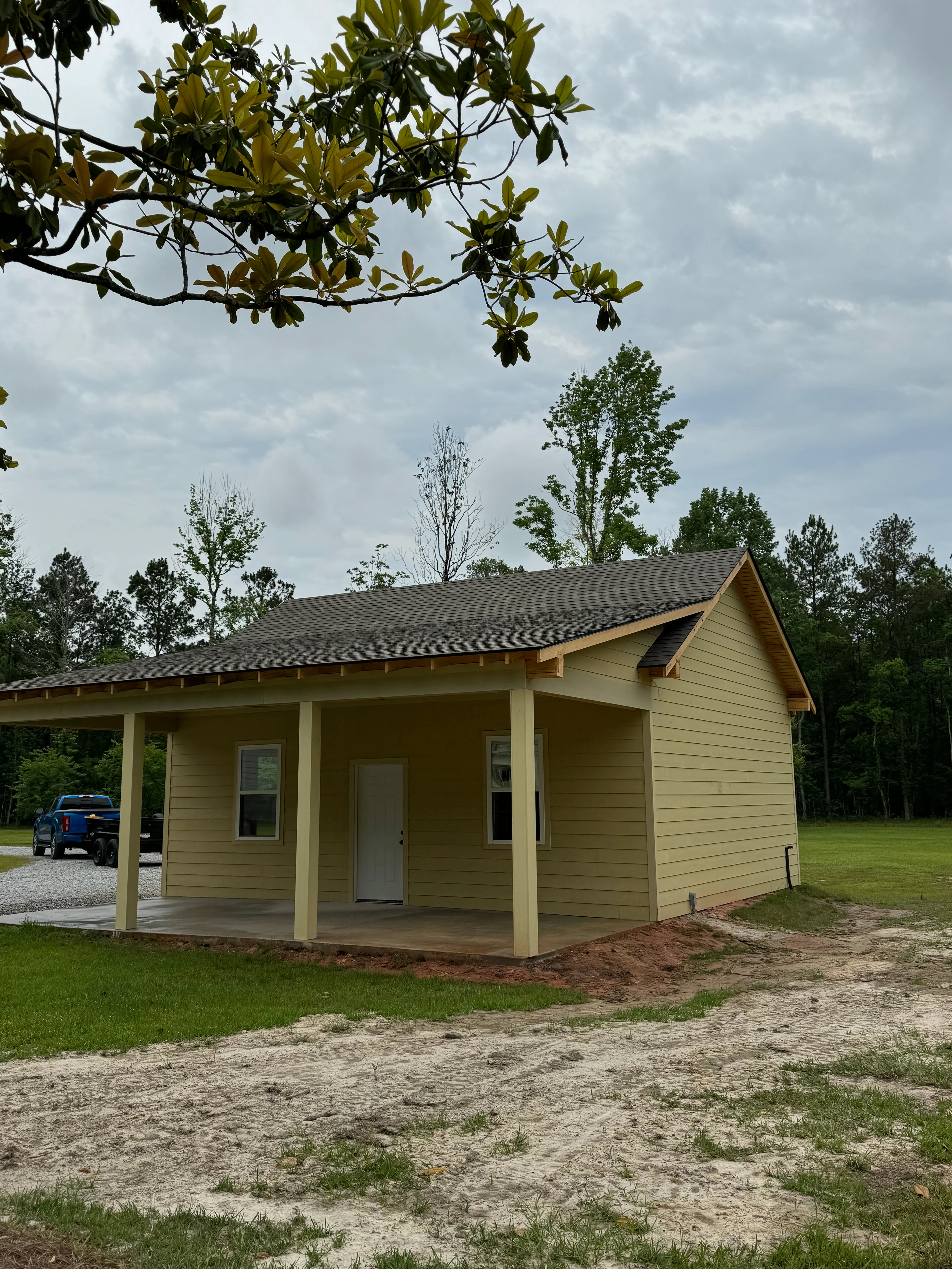 New tan cottage with covered porch and gabled roof in wooded setting