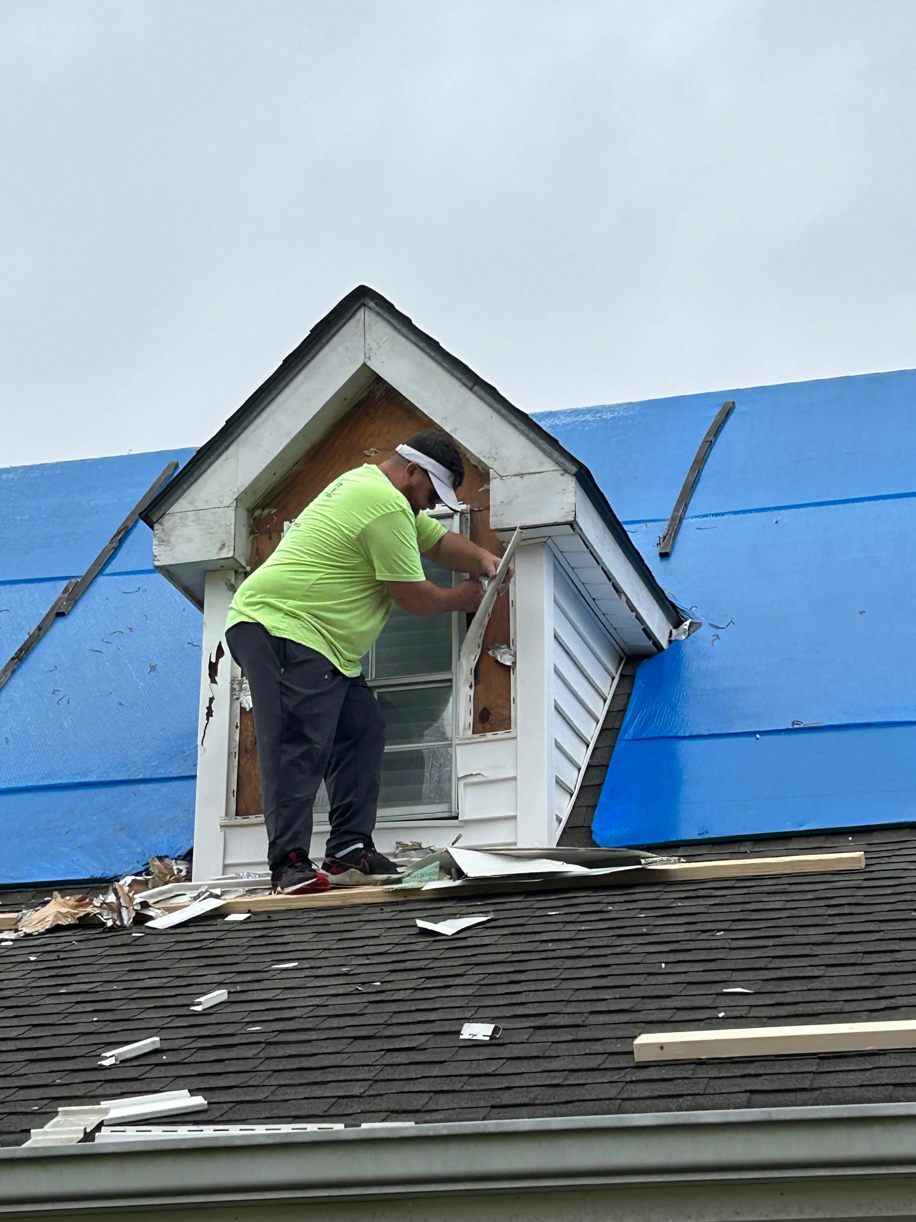 Worker installing white vinyl dormer with new roofing on residential home