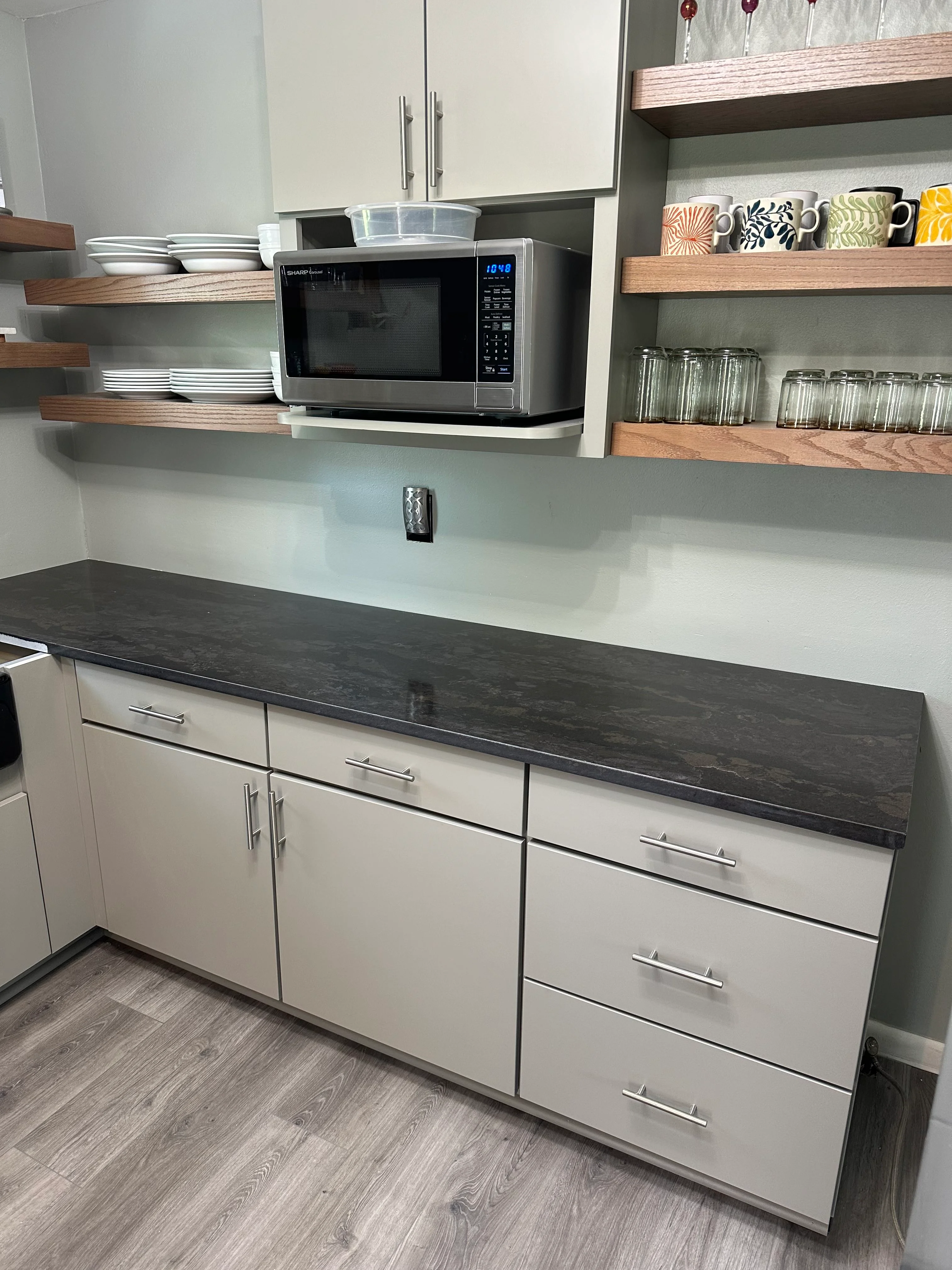 Modern kitchen with white cabinets, dark countertops, open shelving, and stainless steel appliances
