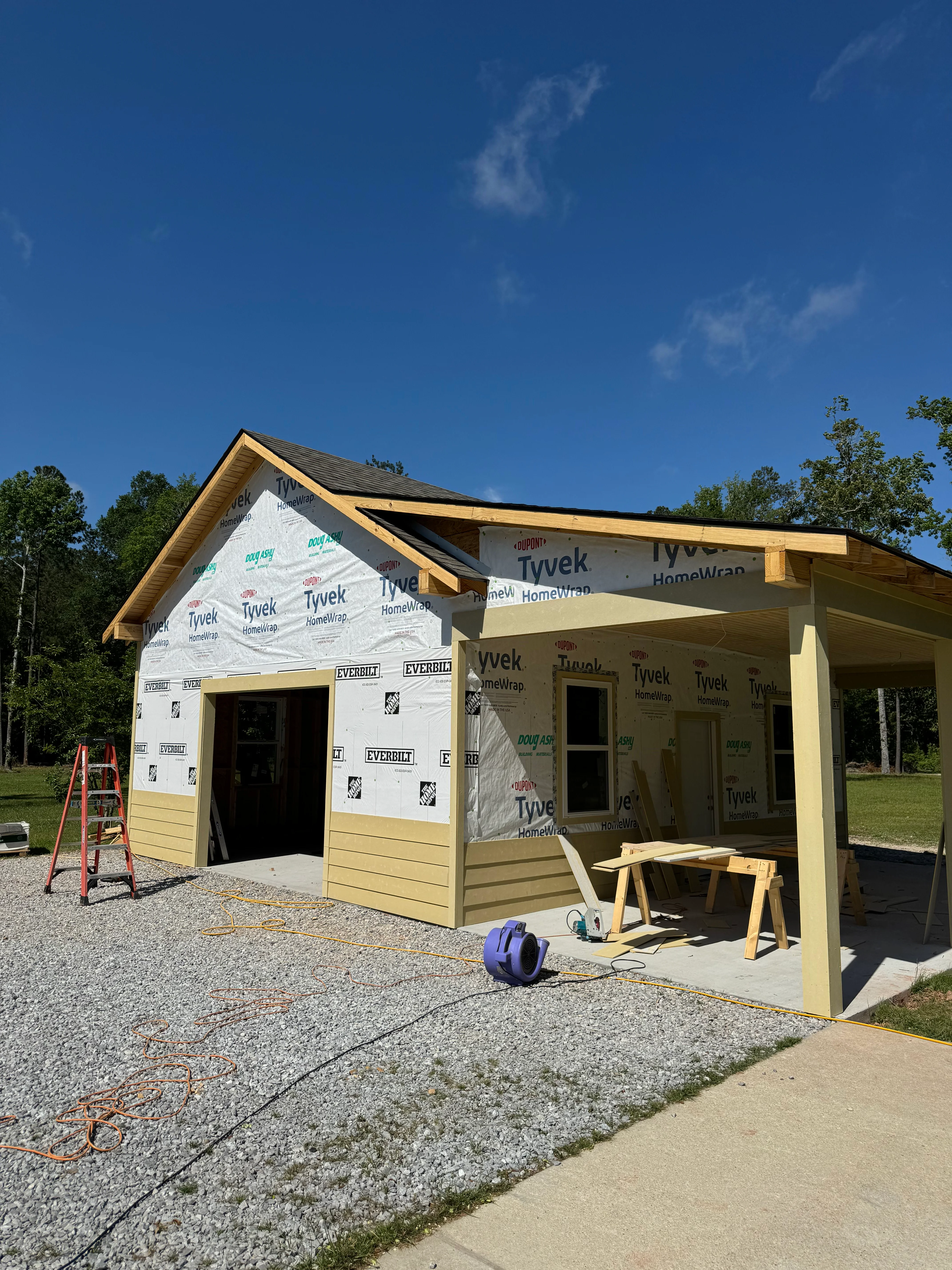 New home under construction with yellow siding, Tyvek wrap, and open porch framing