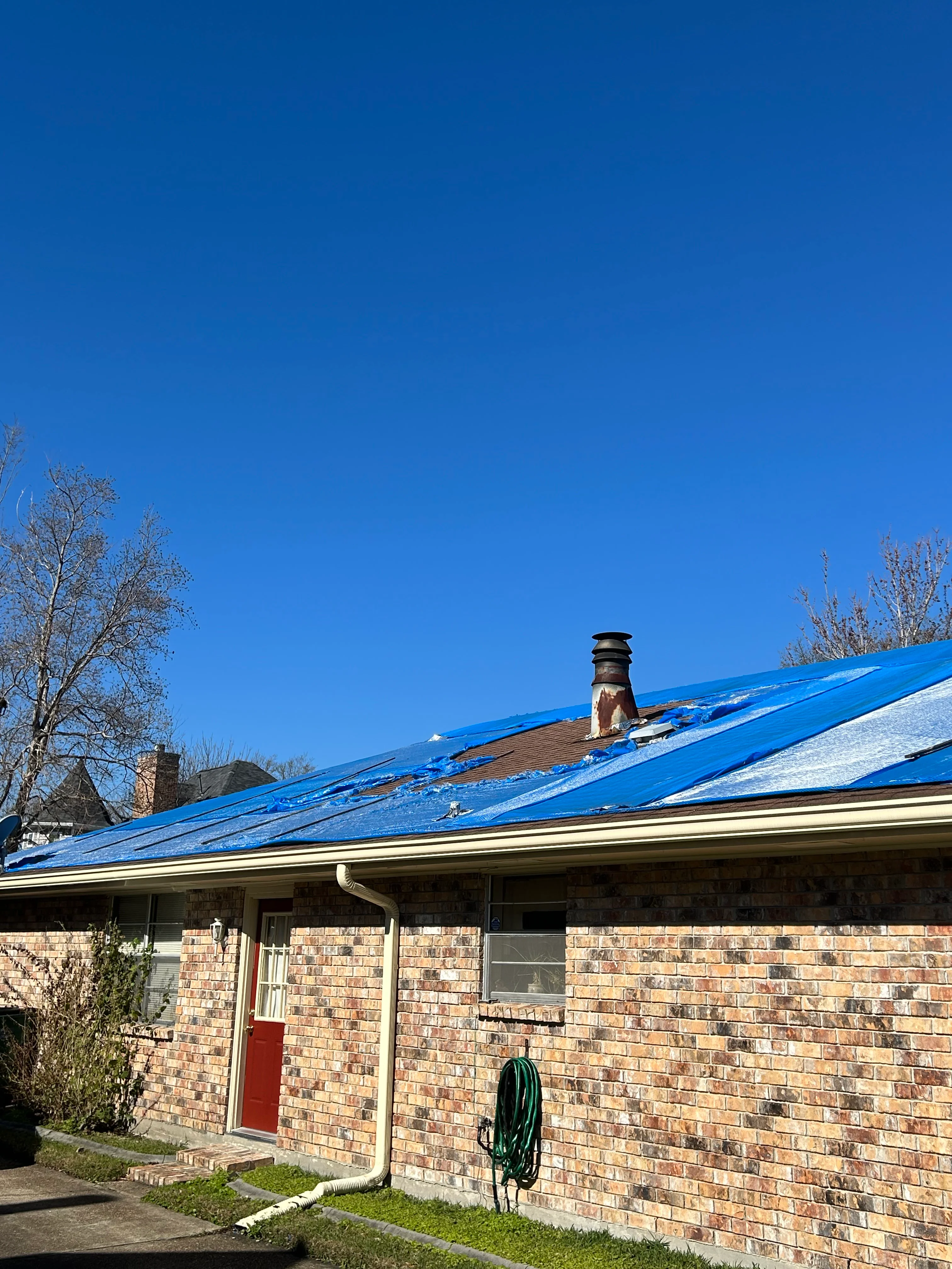 Brick home with newly installed bright blue metal roof and brick chimney against clear sky