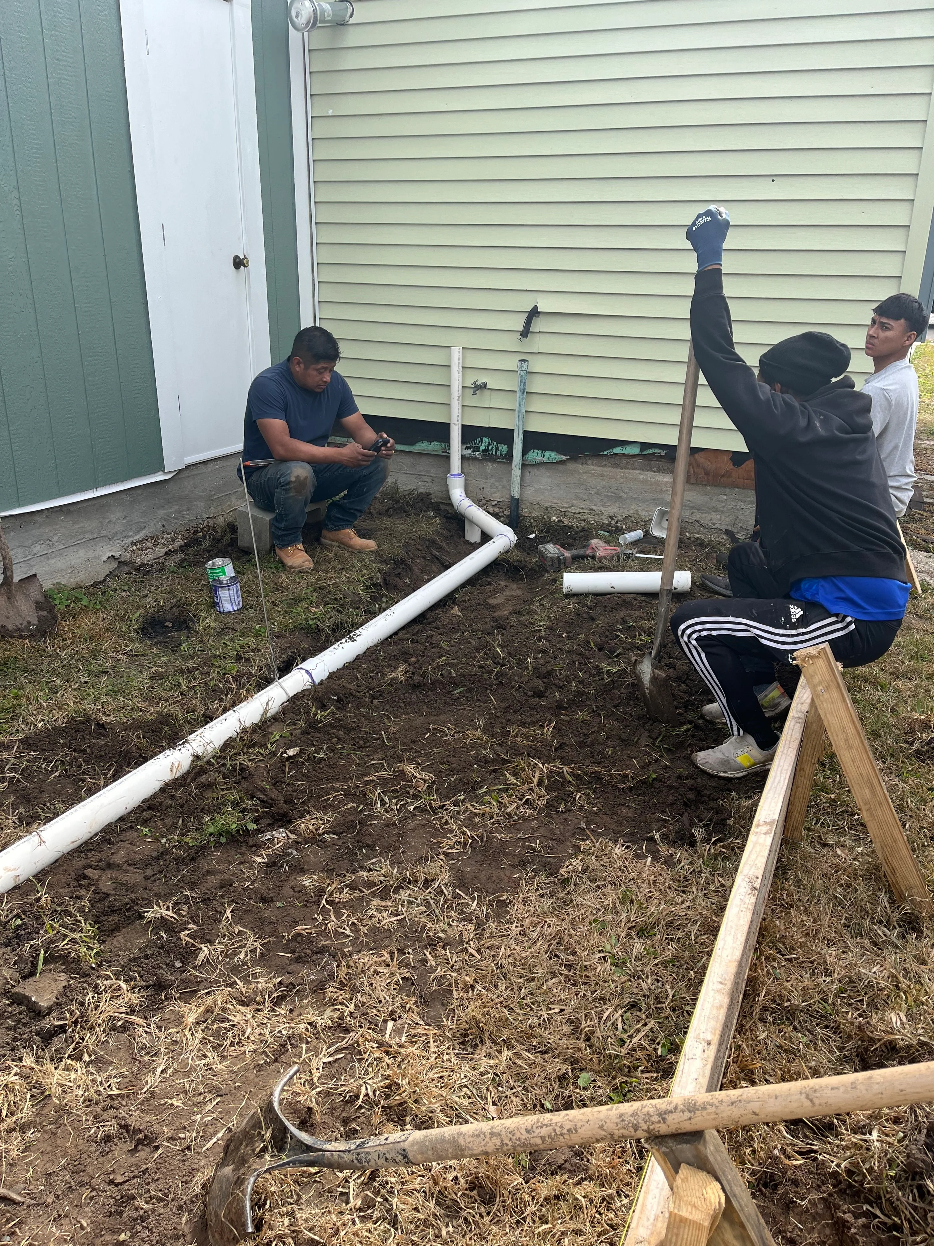 Crew installing white PVC drainage pipes around residential foundation with wooden forms