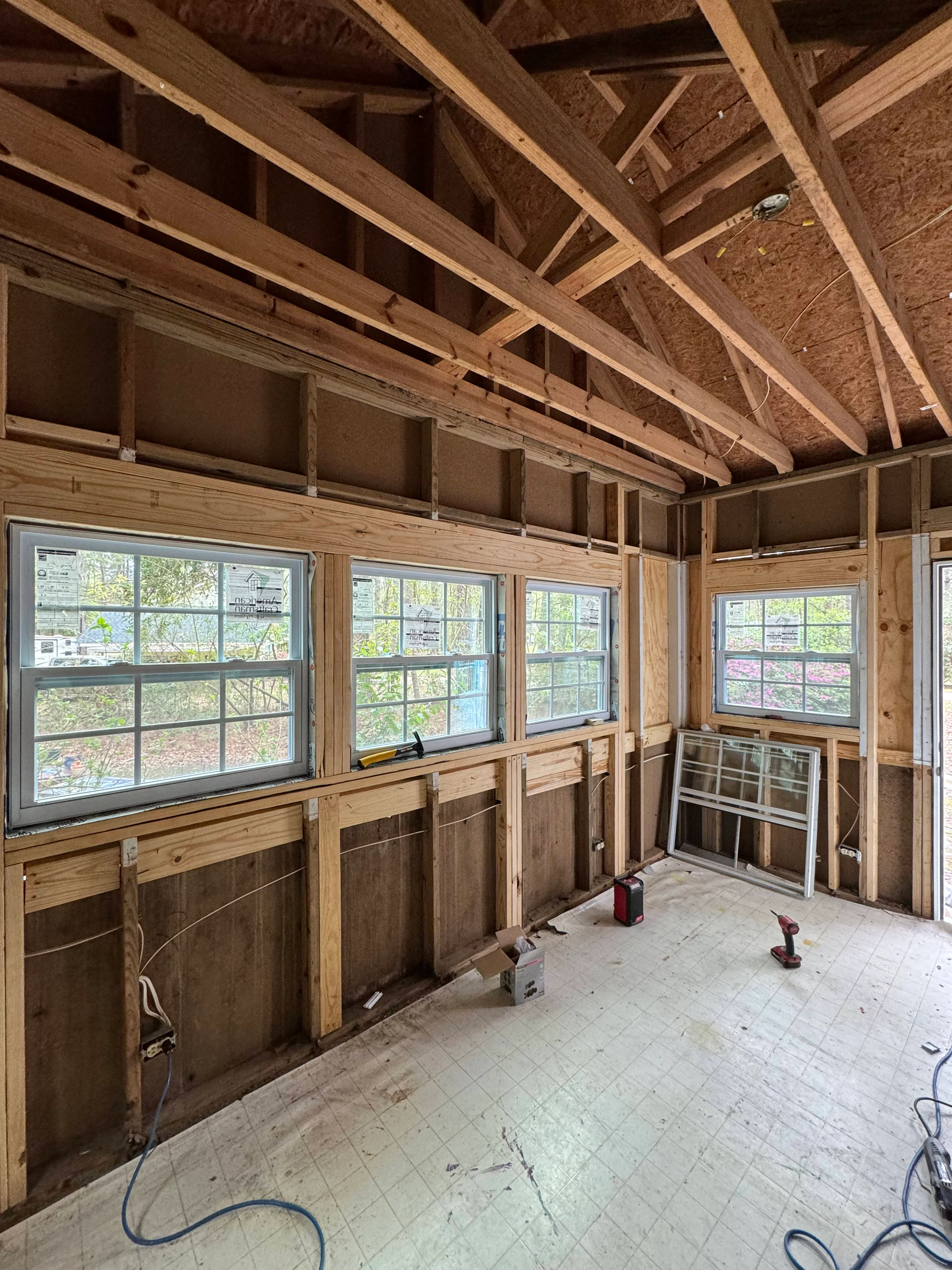 Interior of sunroom under construction with exposed wood beams, multiple windows, and wooden wall framing