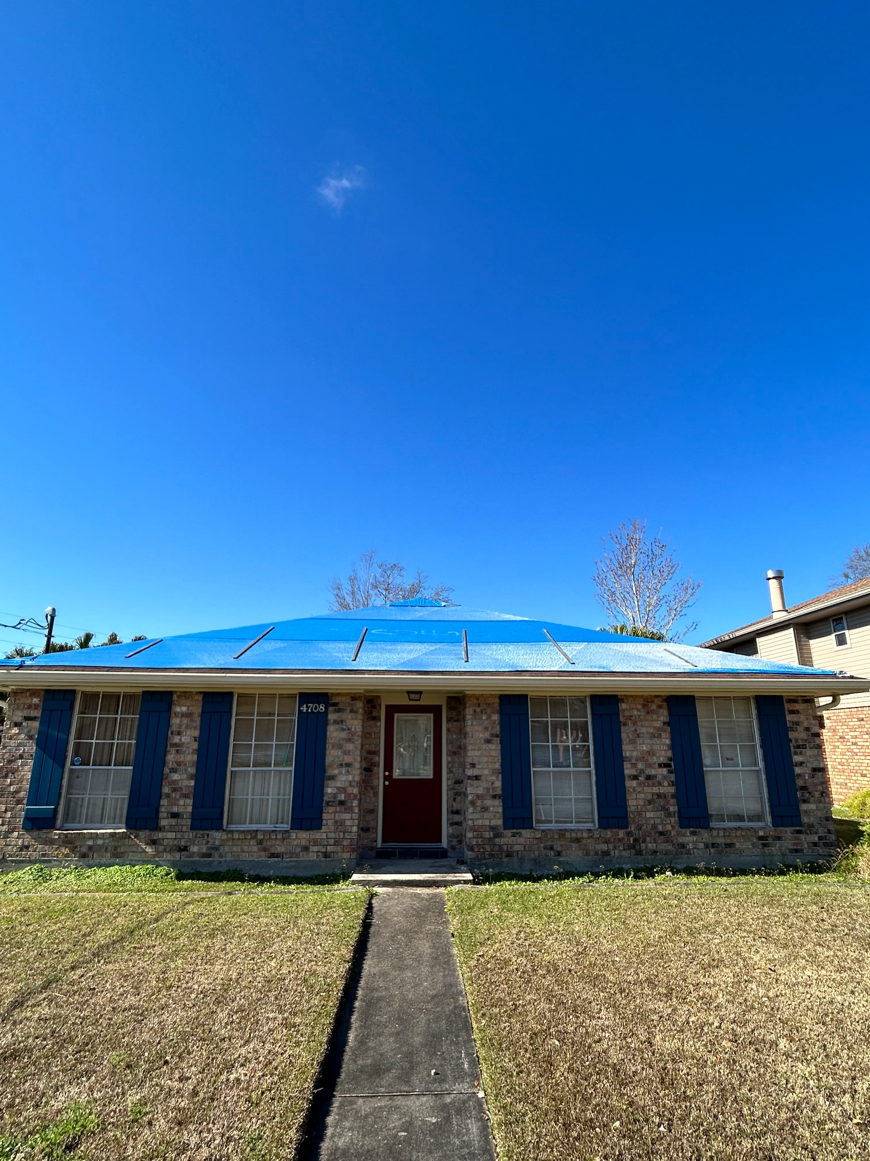 Brick home with new bright blue metal roof and blue shutters in New Orleans