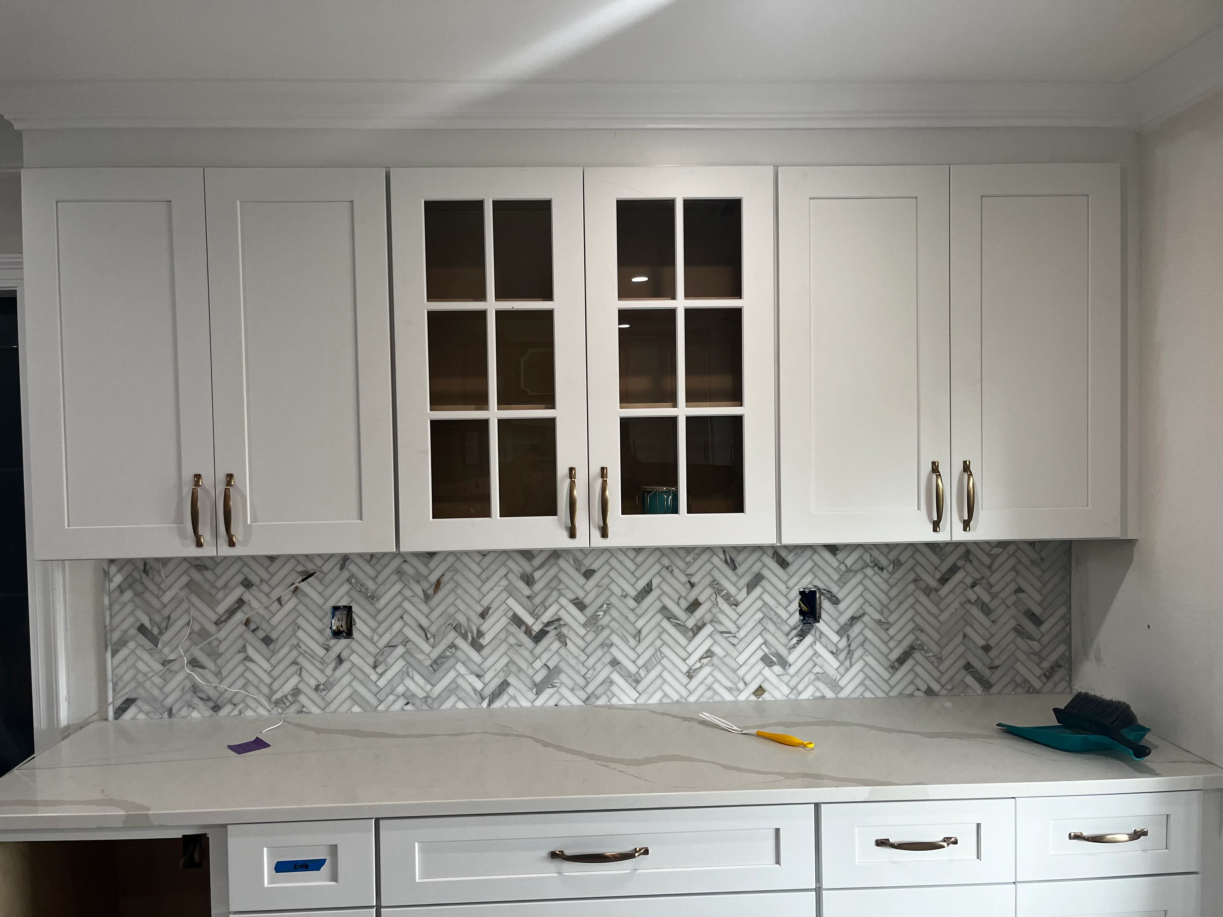 White kitchen cabinets with glass doors and herringbone marble backsplash