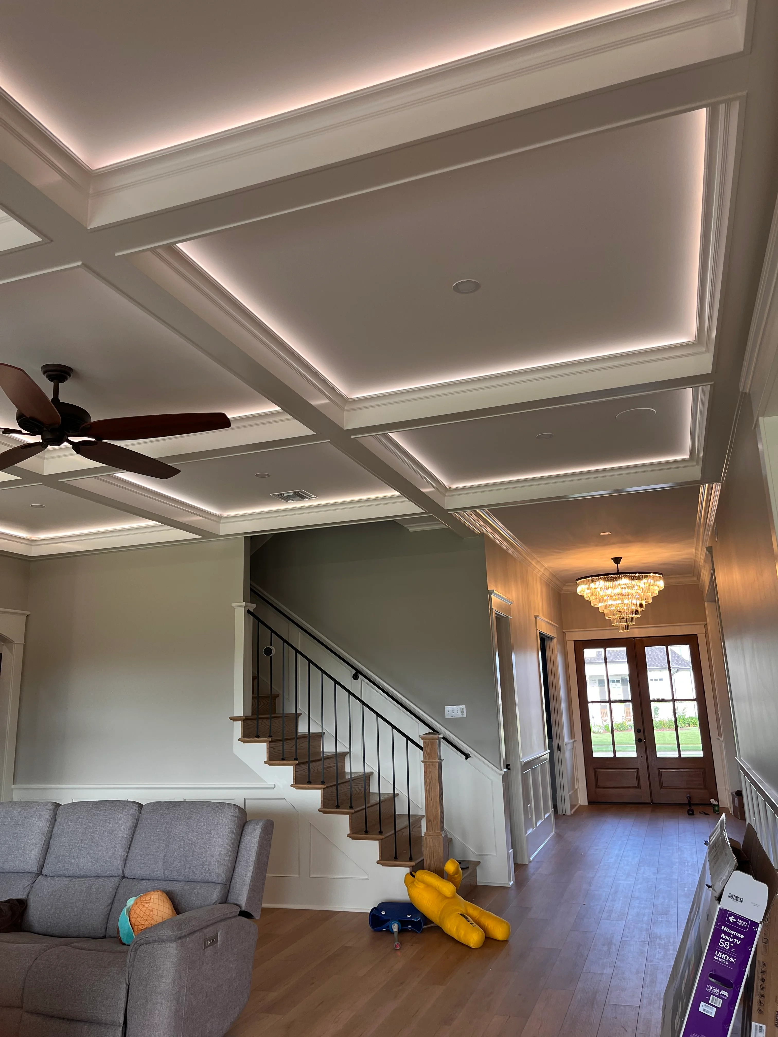 Modern foyer with white coffered ceiling, LED lighting, wooden staircase, and hardwood floors