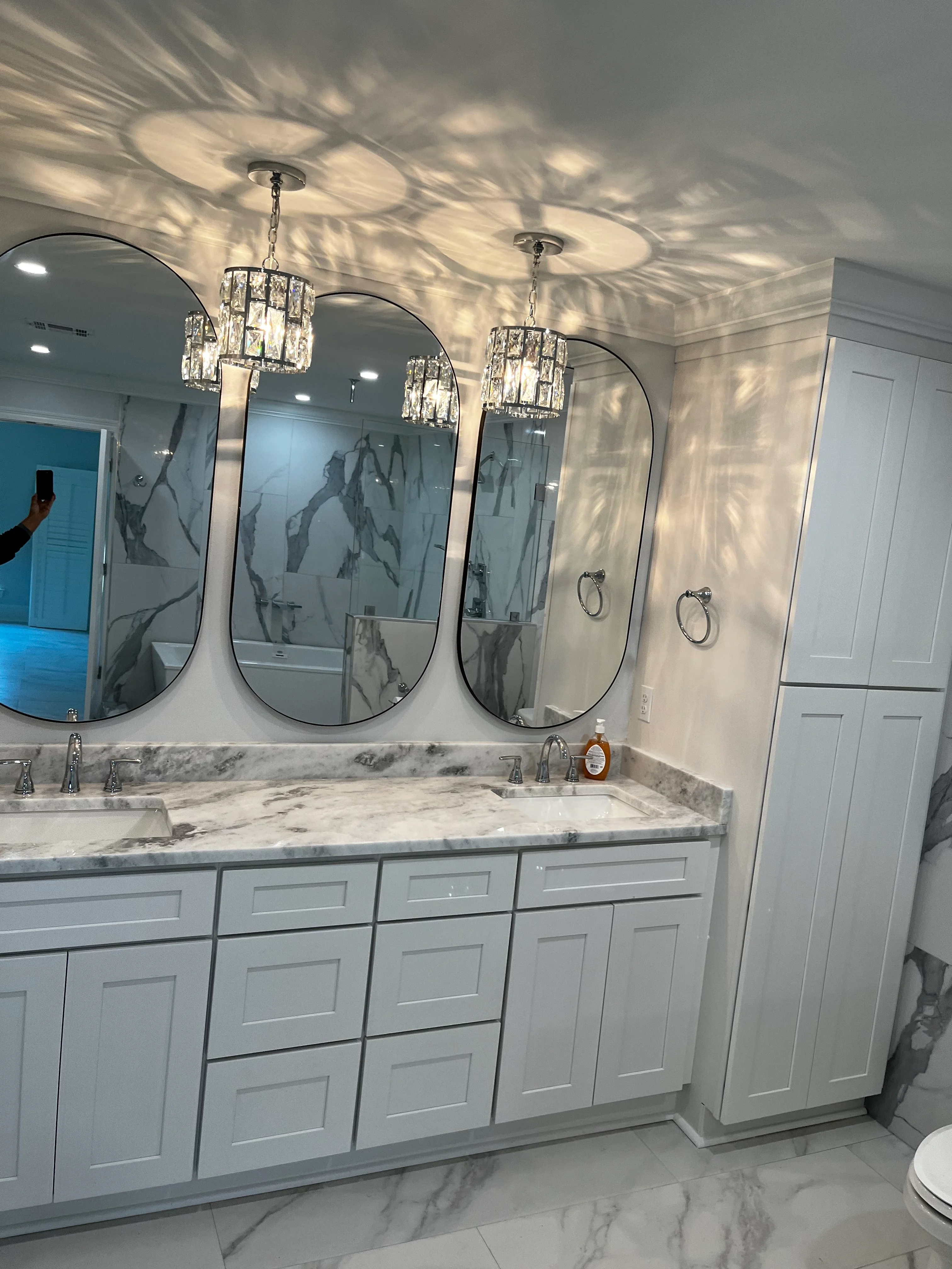Modern master bathroom with white vanity, marble countertop, arched mirrors, and crystal pendant lights