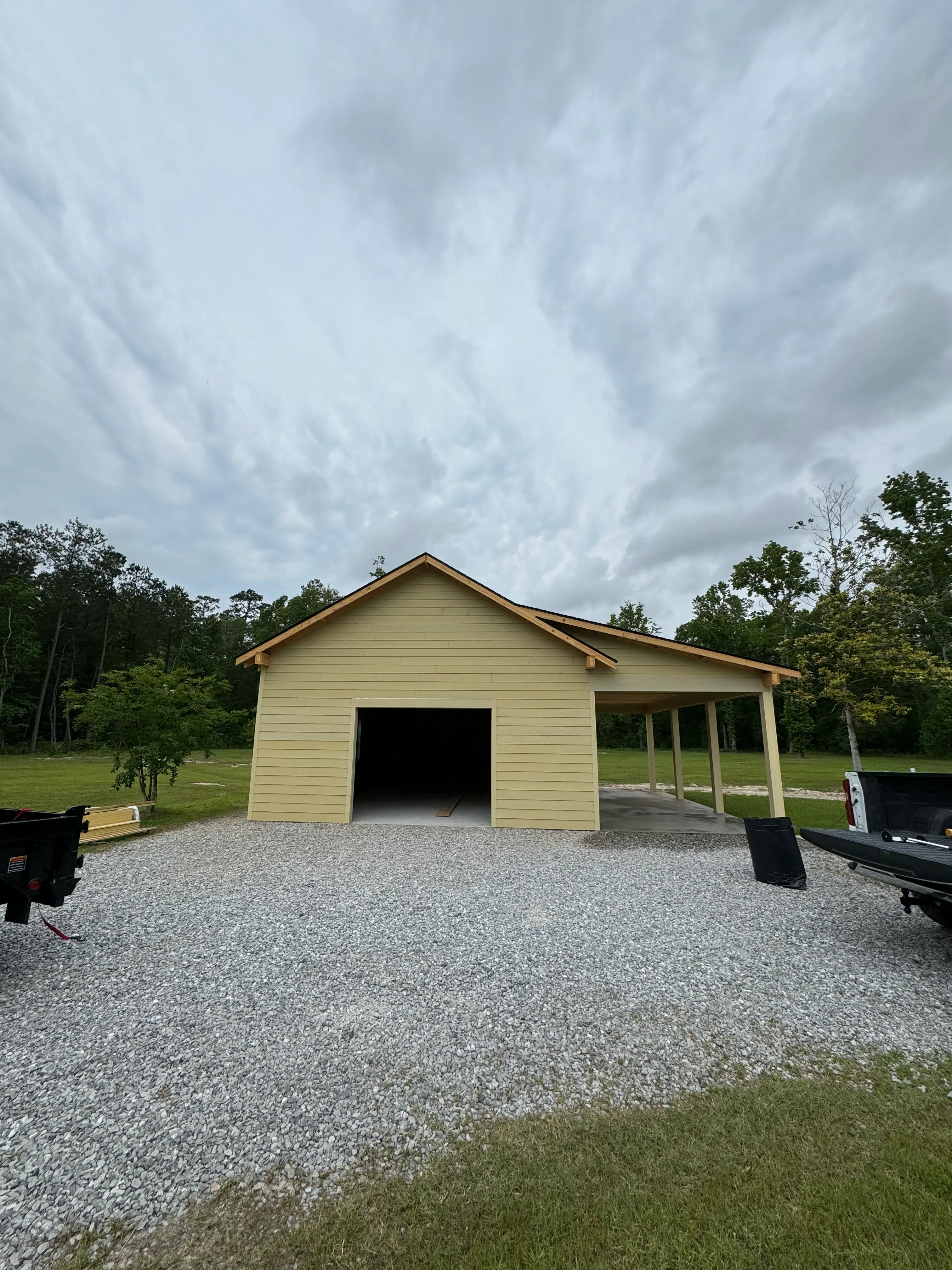 Cream siding garage with gabled roof and open carport on gravel driveway