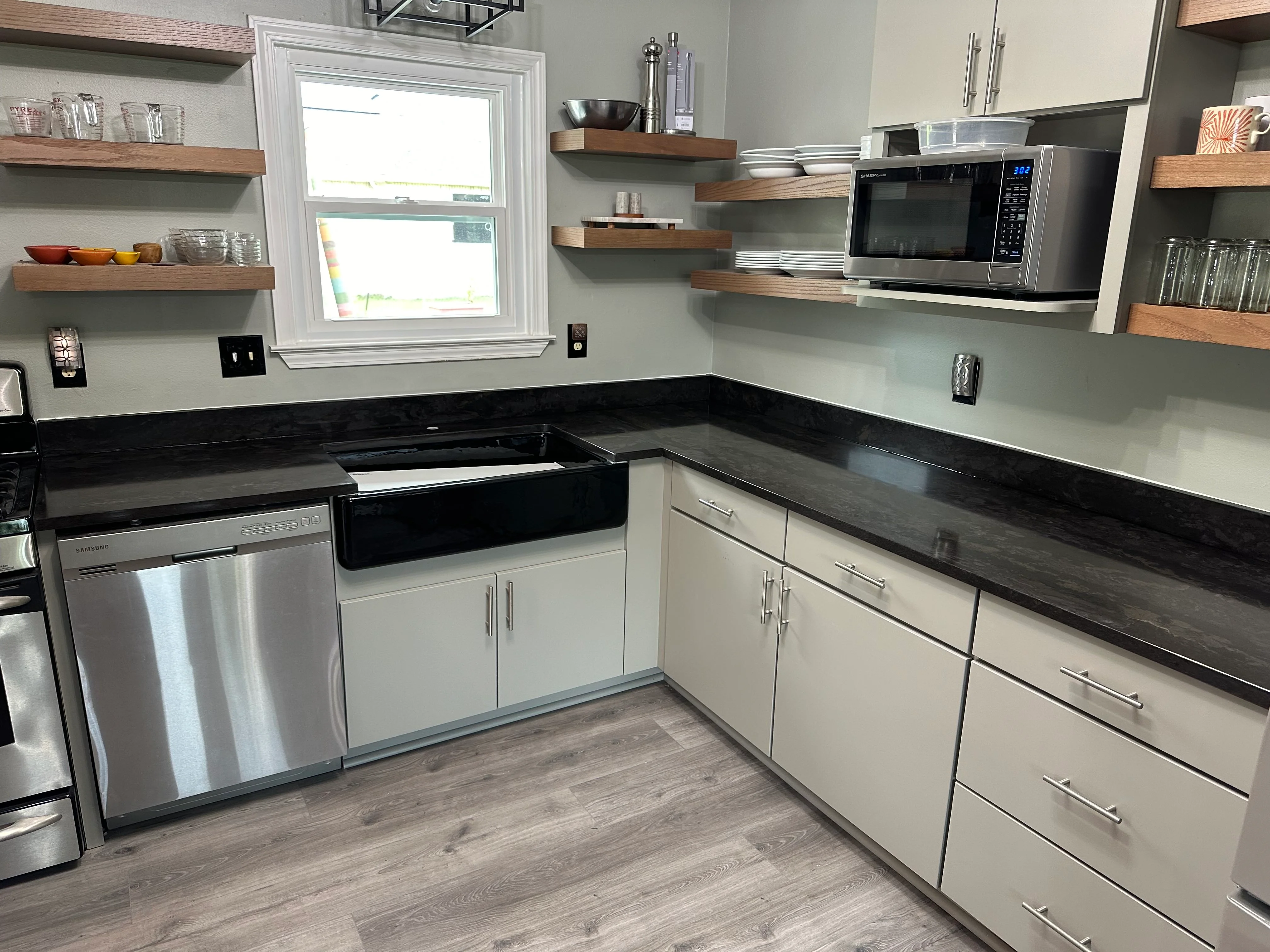 Modern kitchen with white cabinets, black quartz counters, and wood floating shelves