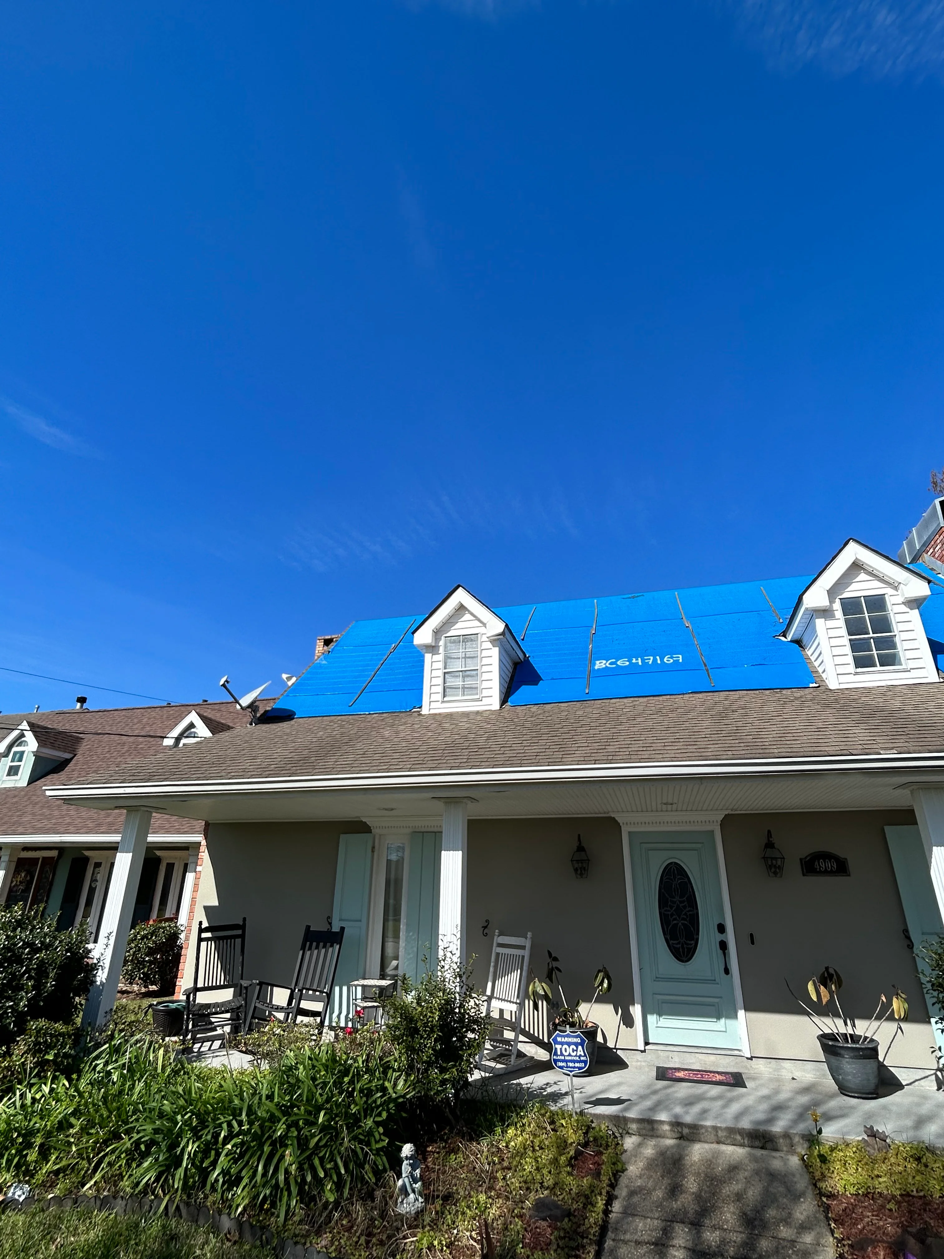 Home with blue roofing underlayment and two white dormers under clear sky