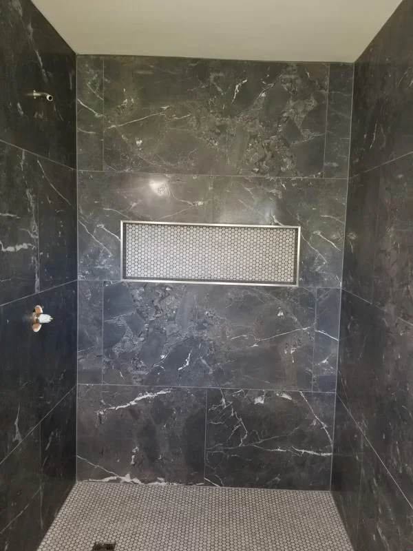Black marble tile shower enclosure with linear drain and penny-round floor tiles