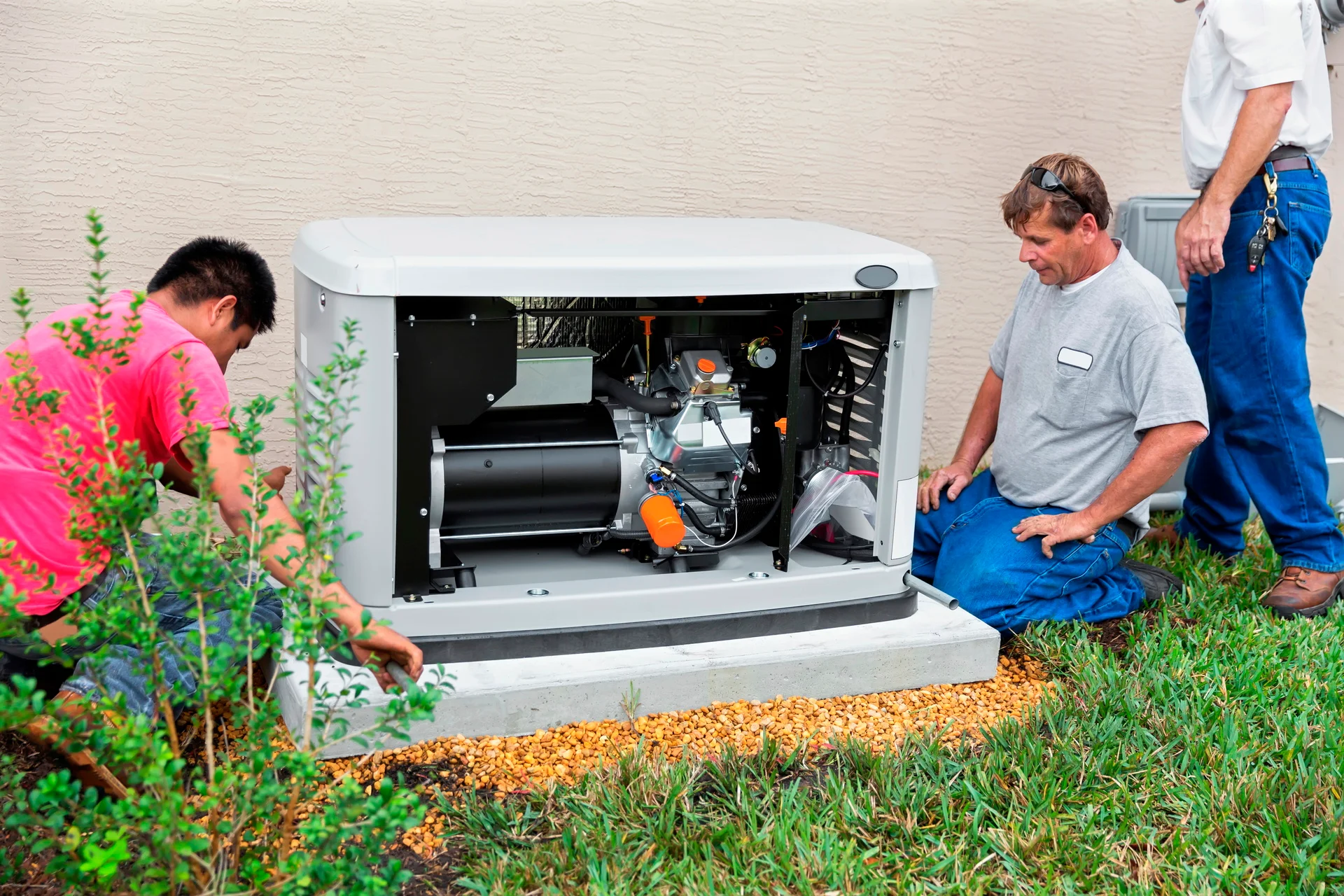 Technicians installing white residential standby generator with visible engine components and orange accents