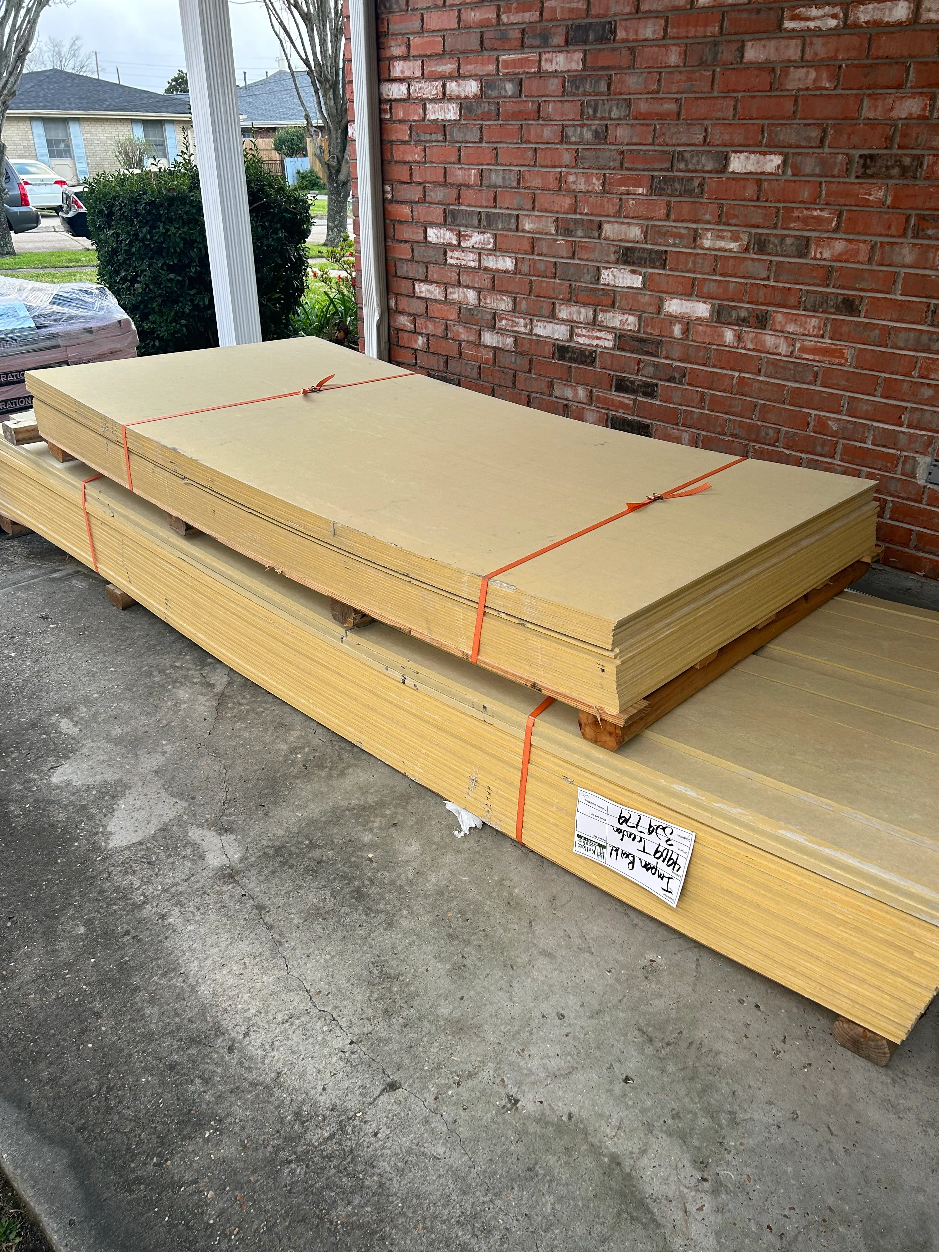 Stacked yellow lumber bundles with orange straps on residential driveway