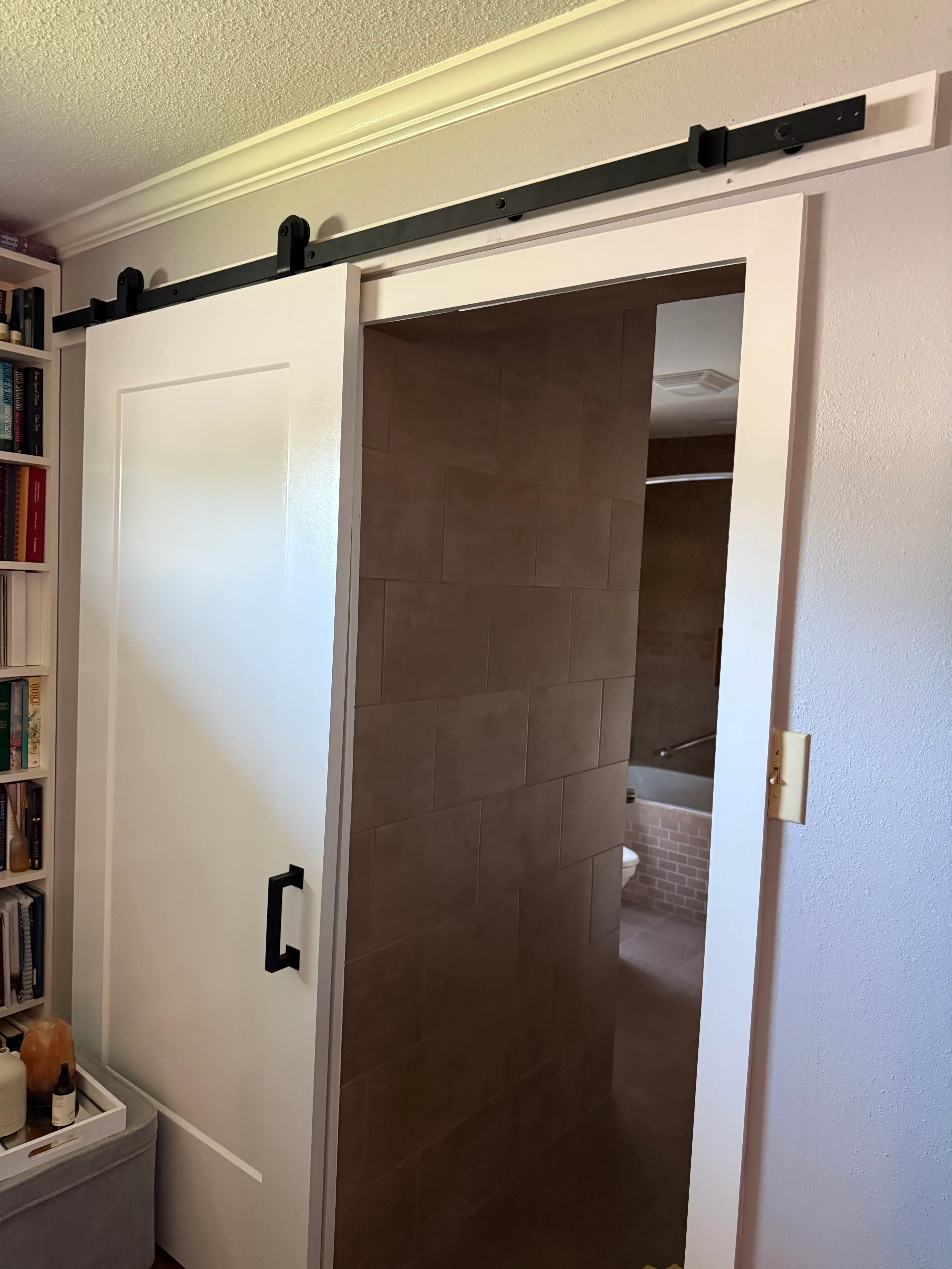 Dark brown sliding barn door with black hardware track mounted on white wall frame