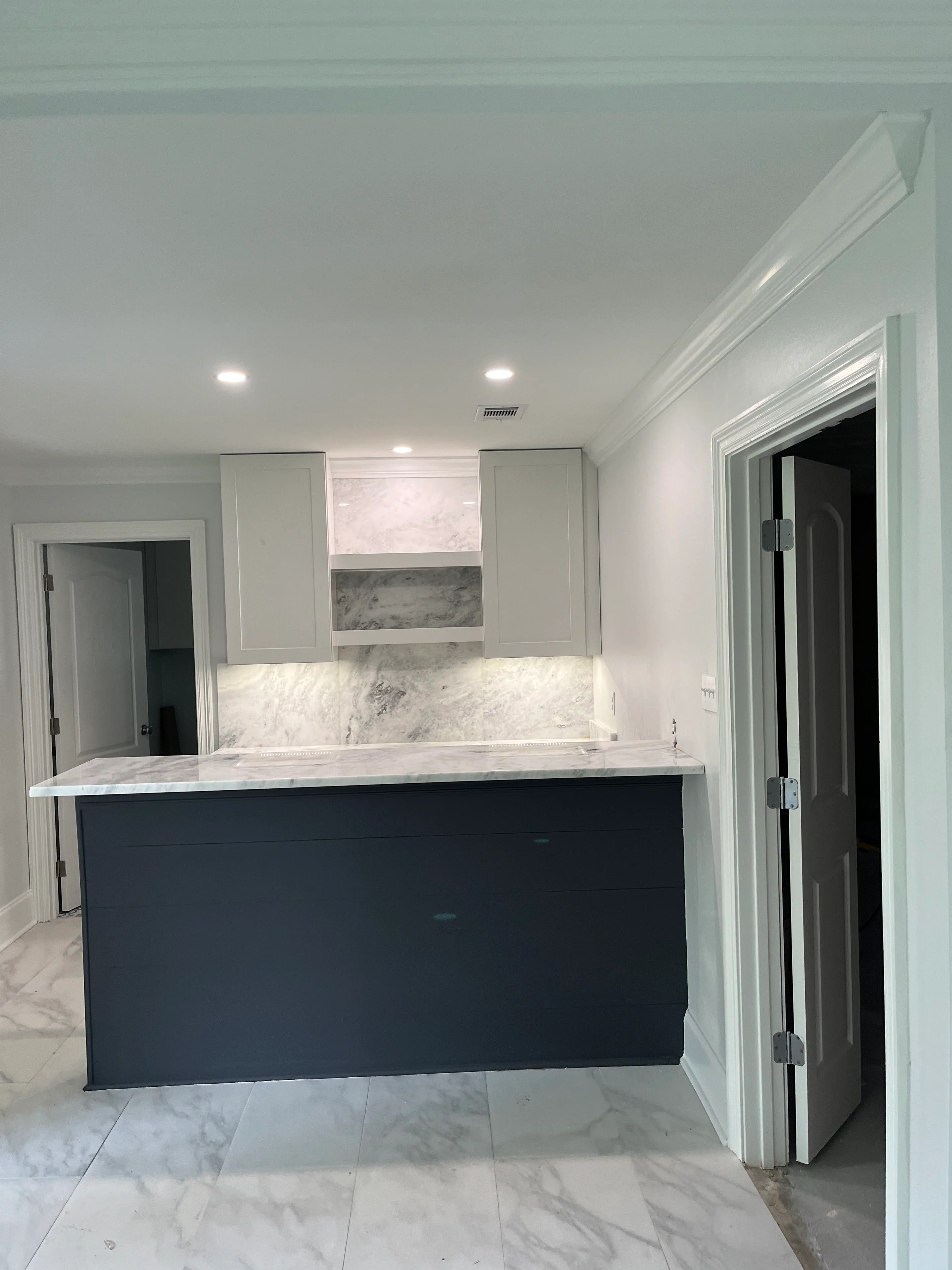 Modern kitchen with white cabinets, marble backsplash, dark island, and marble flooring