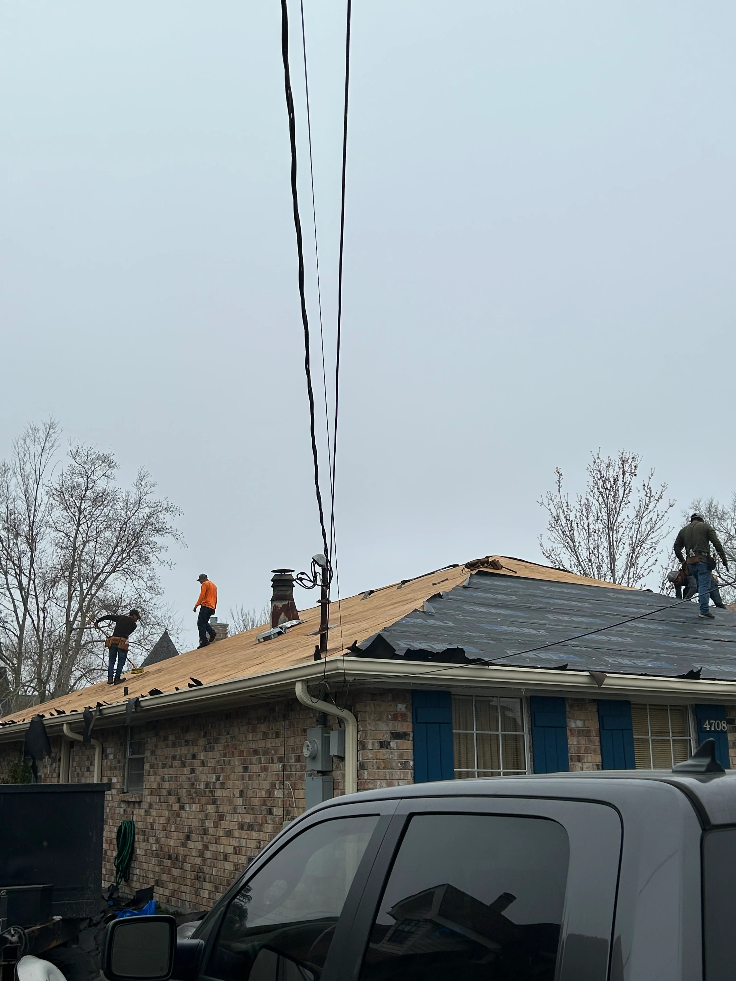 Roofing crew installing new asphalt shingles on brick residential home
