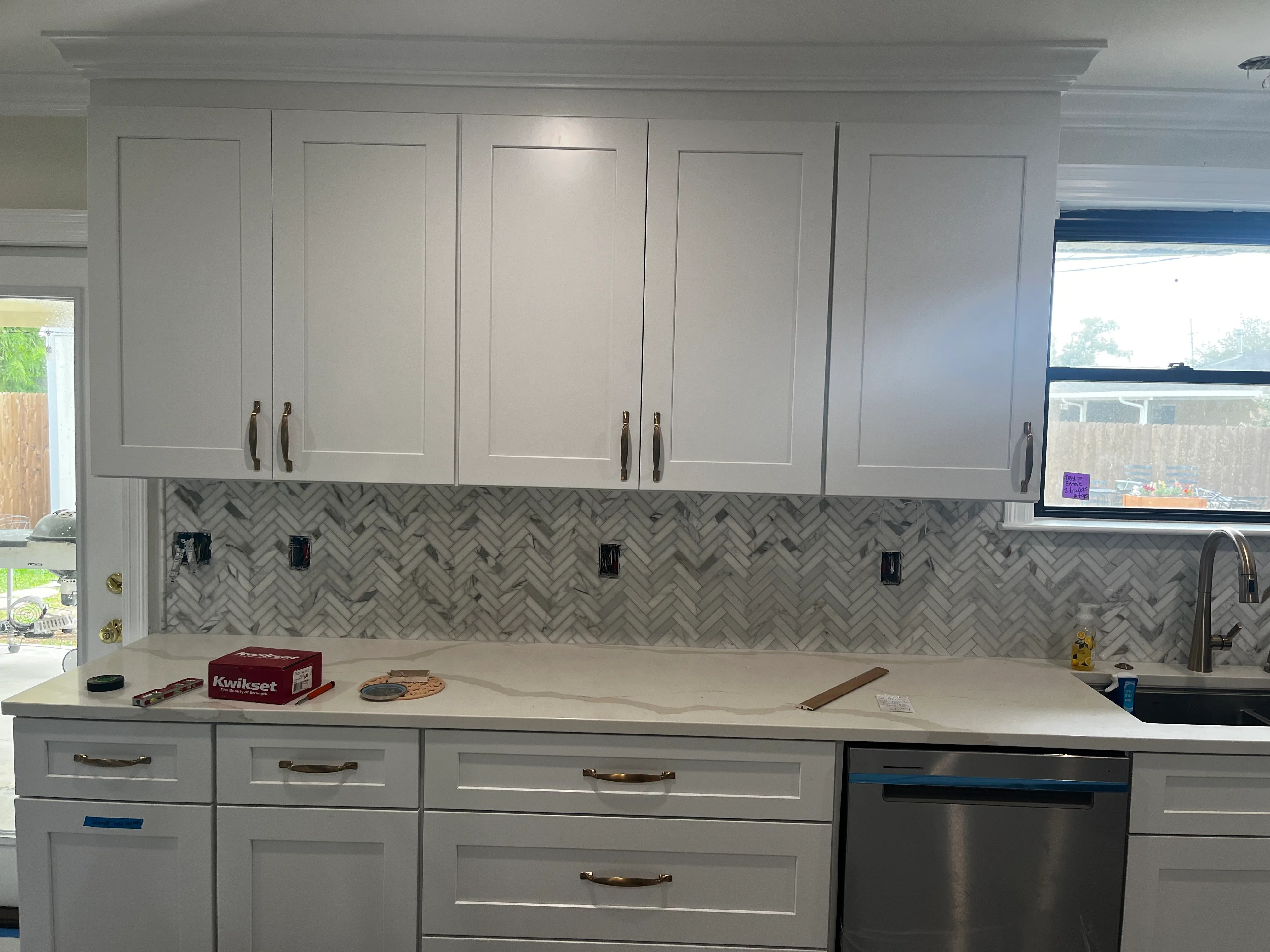 Modern kitchen with white cabinetry, herringbone tile backsplash, and quartz countertops
