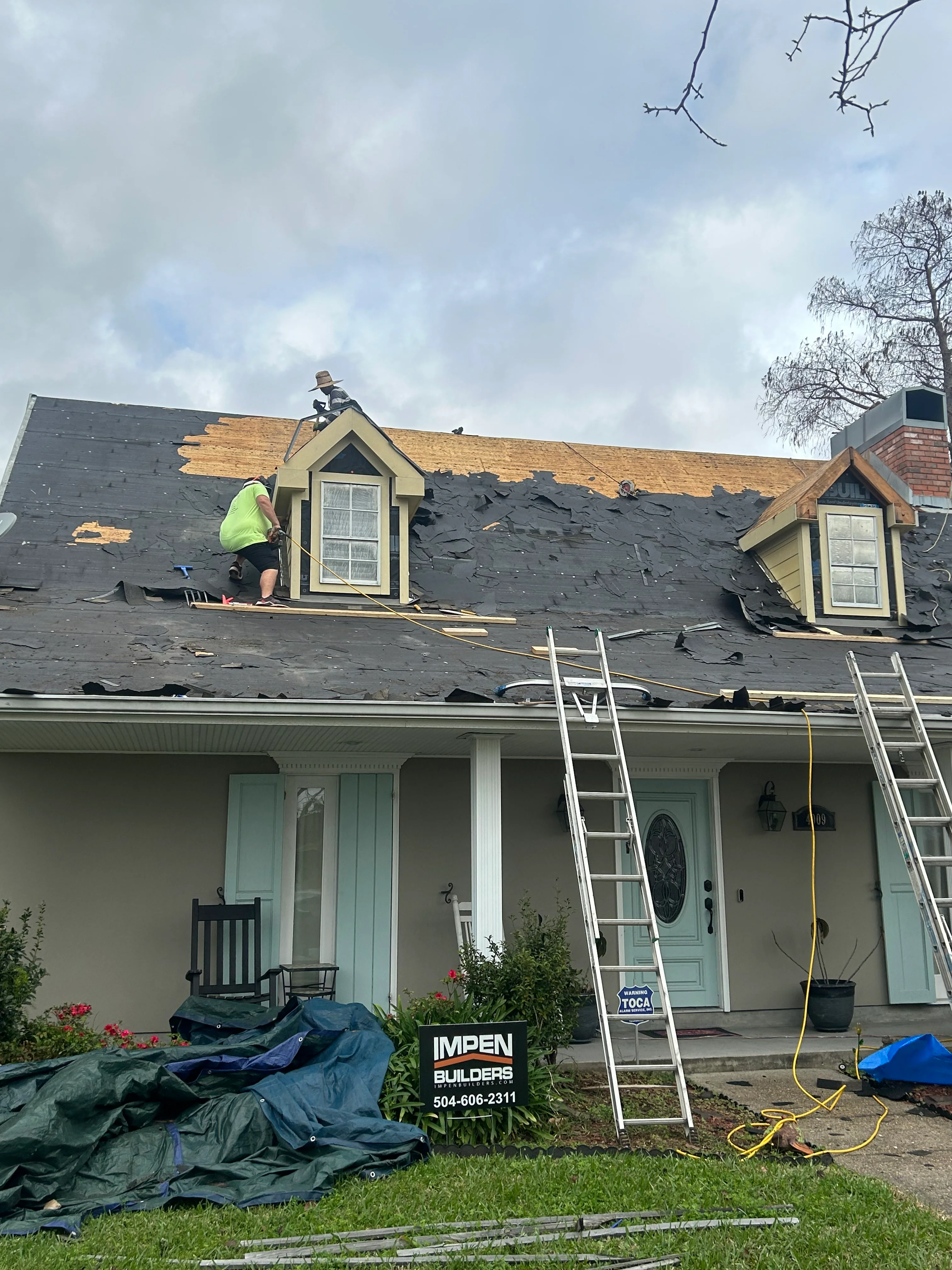 Roofers installing new shingles on residential home with exposed wood decking and dormer windows
