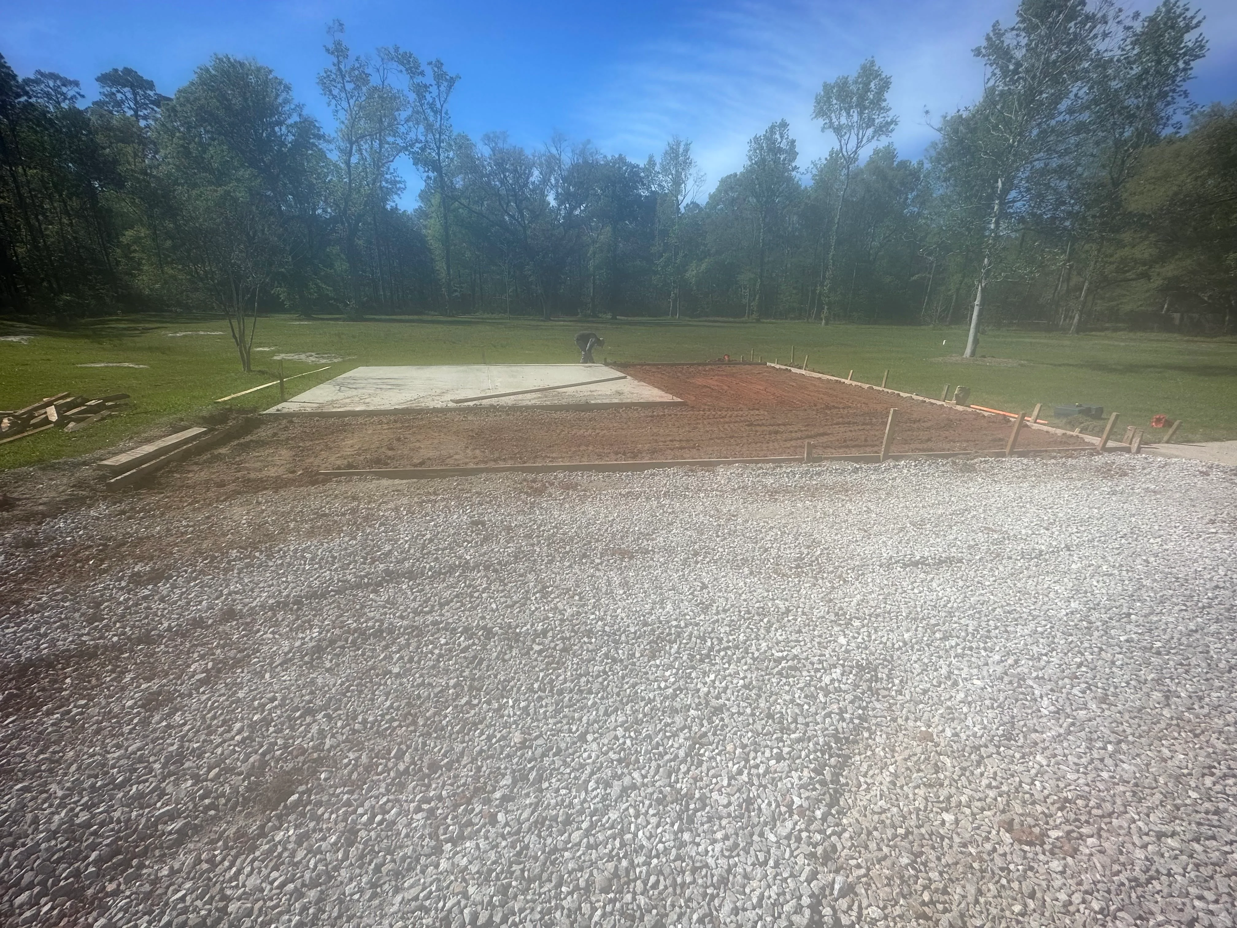 Gravel arena base with concrete pad and wooden boundary markers in wooded setting