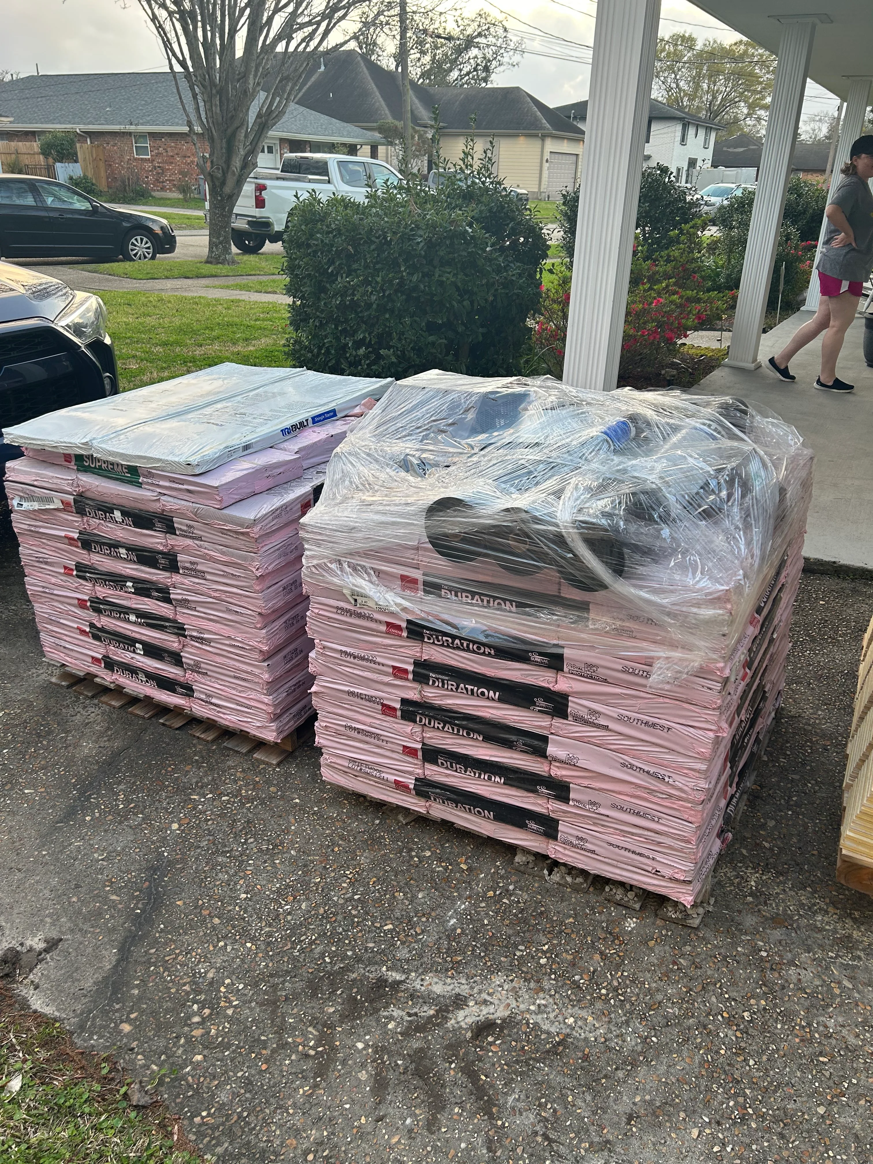 Stacked pink roofing insulation boards and wrapped materials on pallets under carport