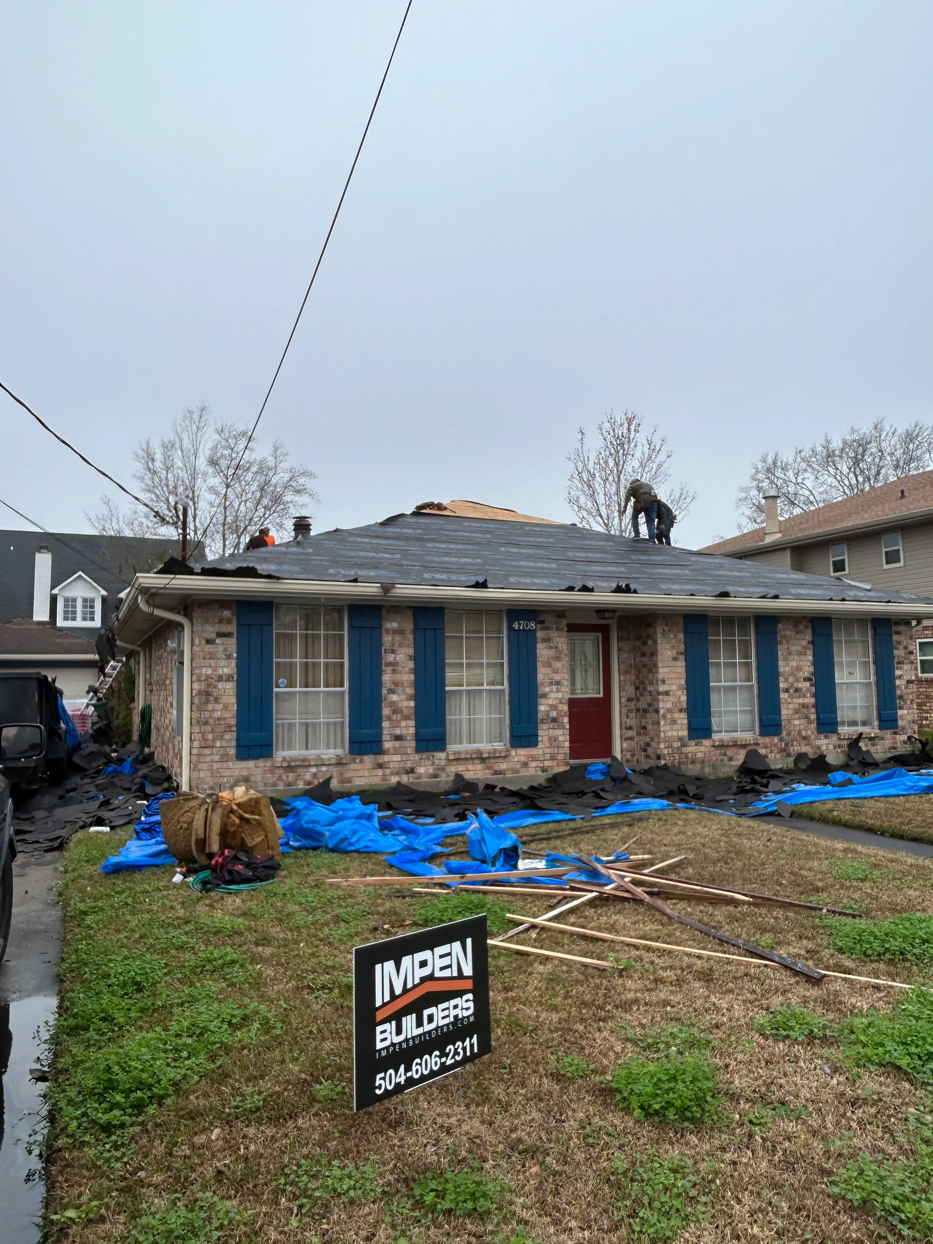 Brick home with new dark roof shingles being installed, protective blue tarps covering yard