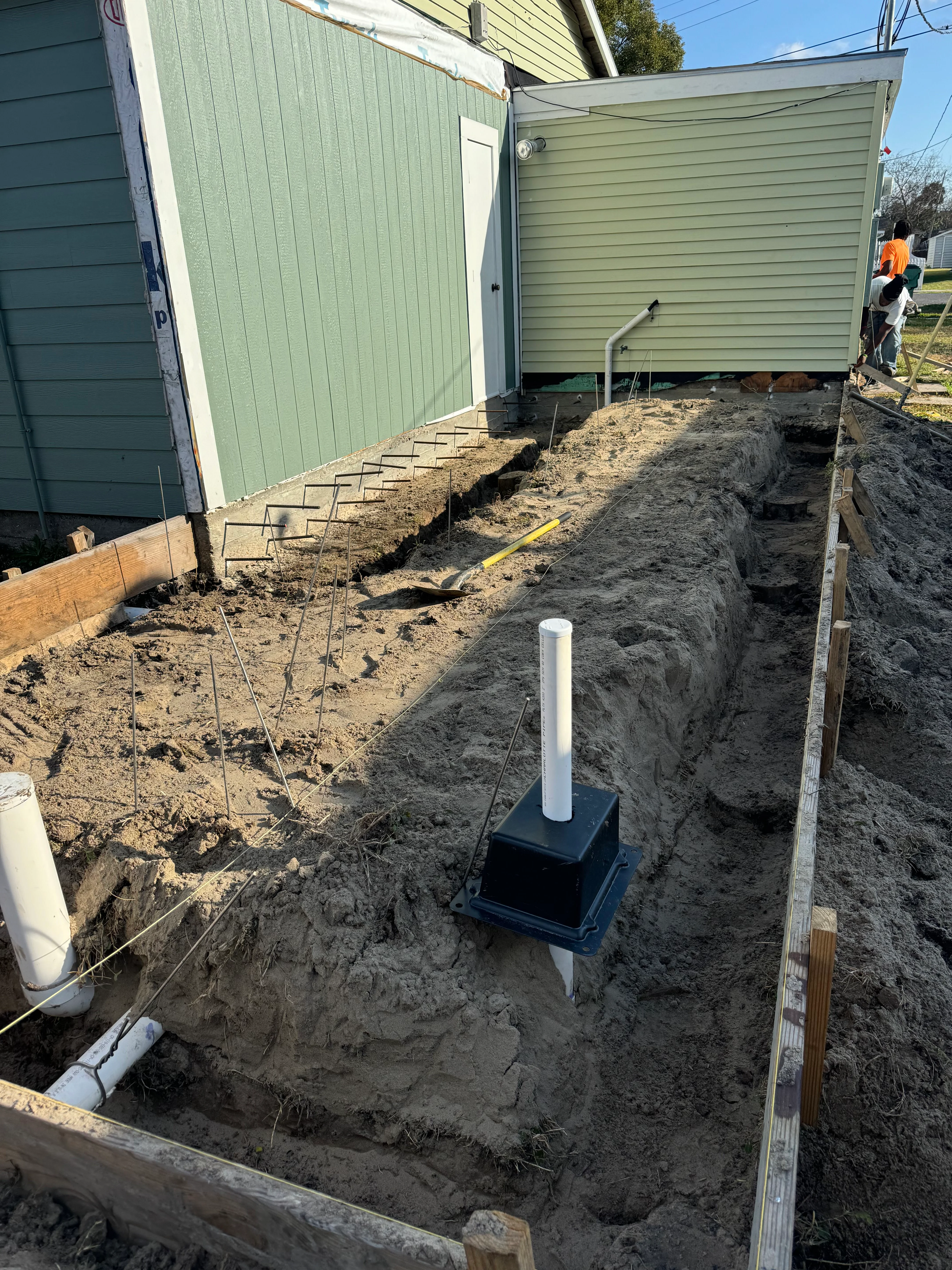 Excavated septic system installation with tank vault and underground piping between metal-sided buildings