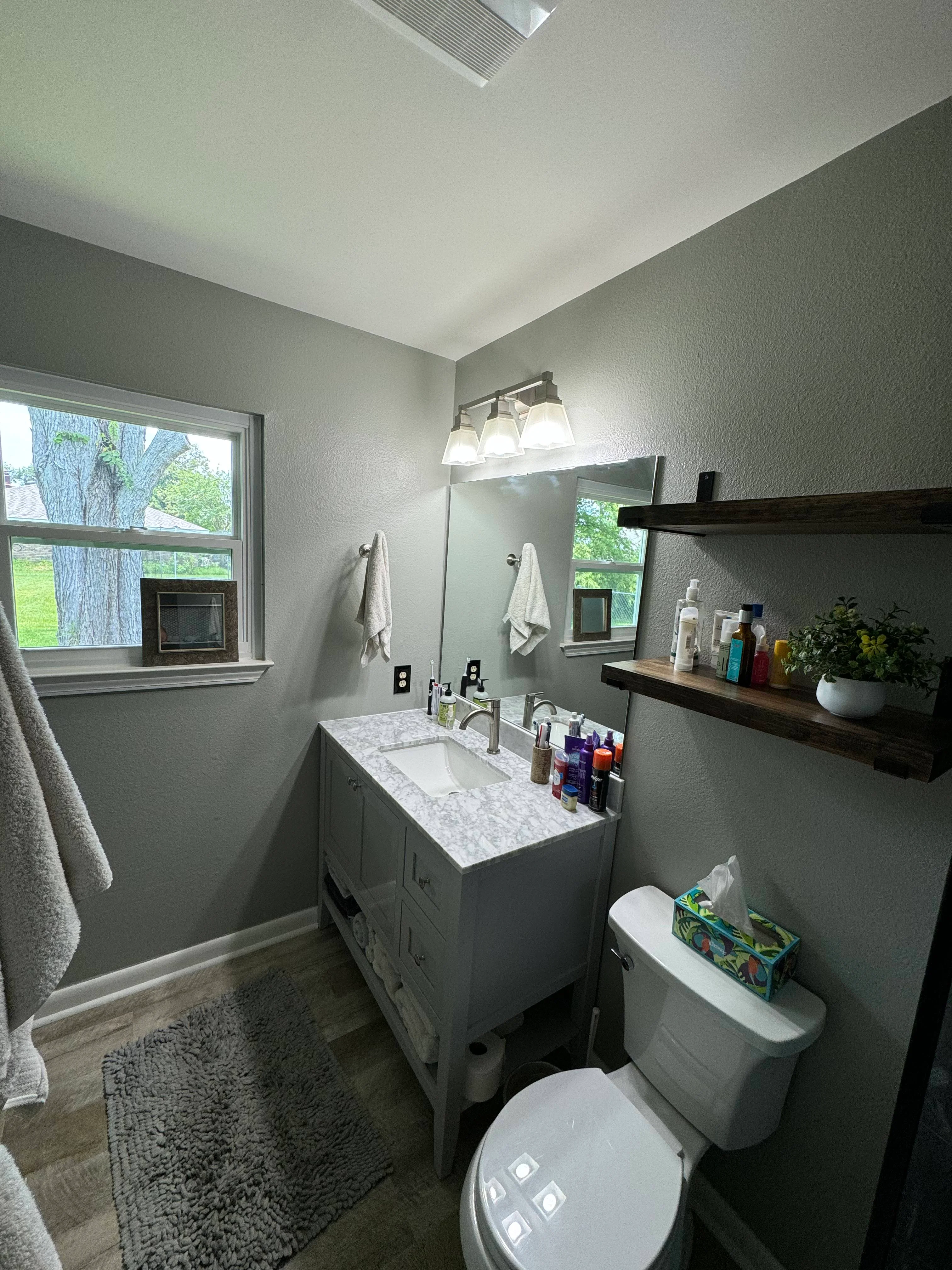 Modern bathroom with white vanity, marble countertop, mirror, and gray walls with natural light from windows