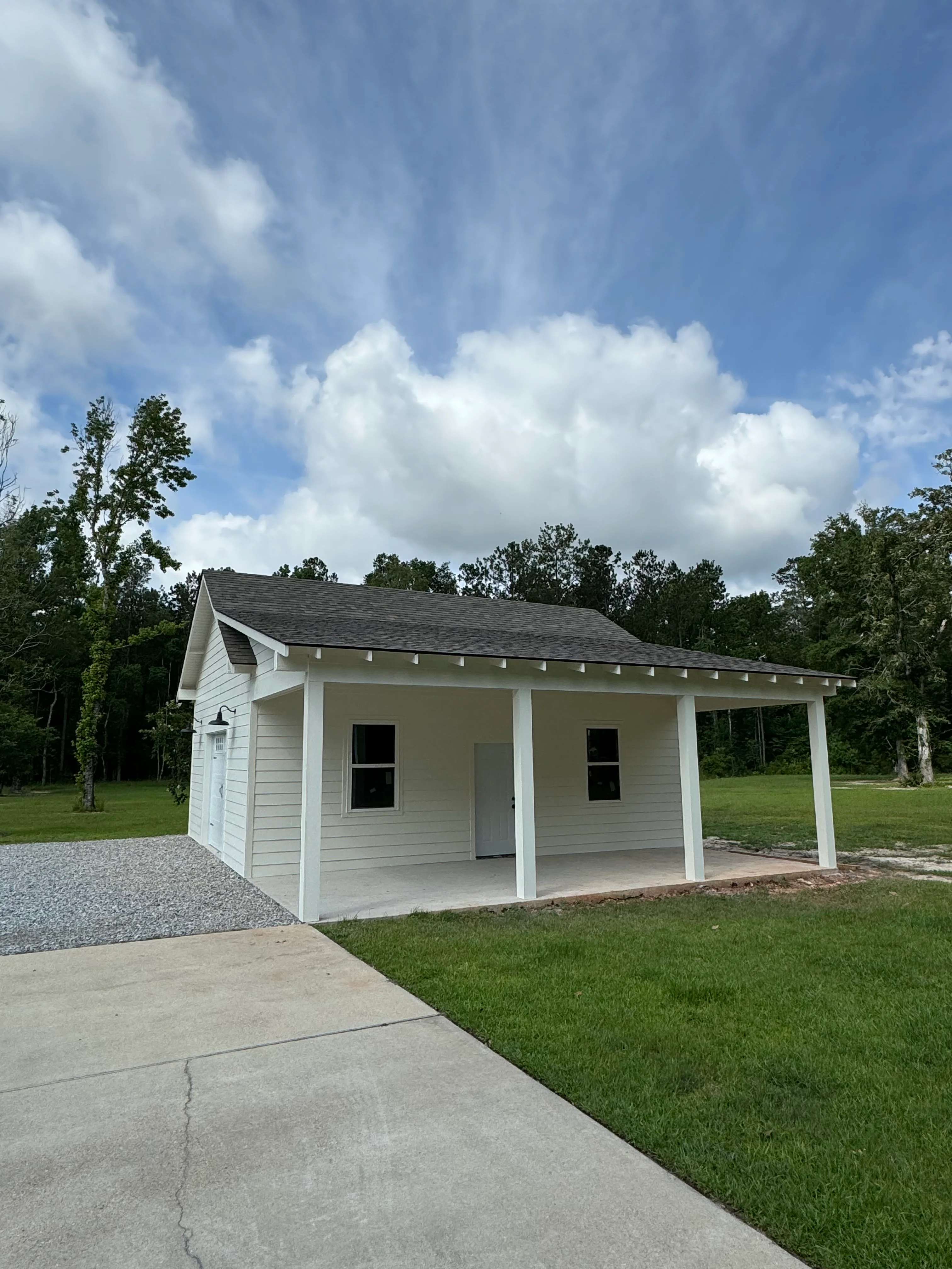 White cottage with covered porch and dark roof on grassy lot