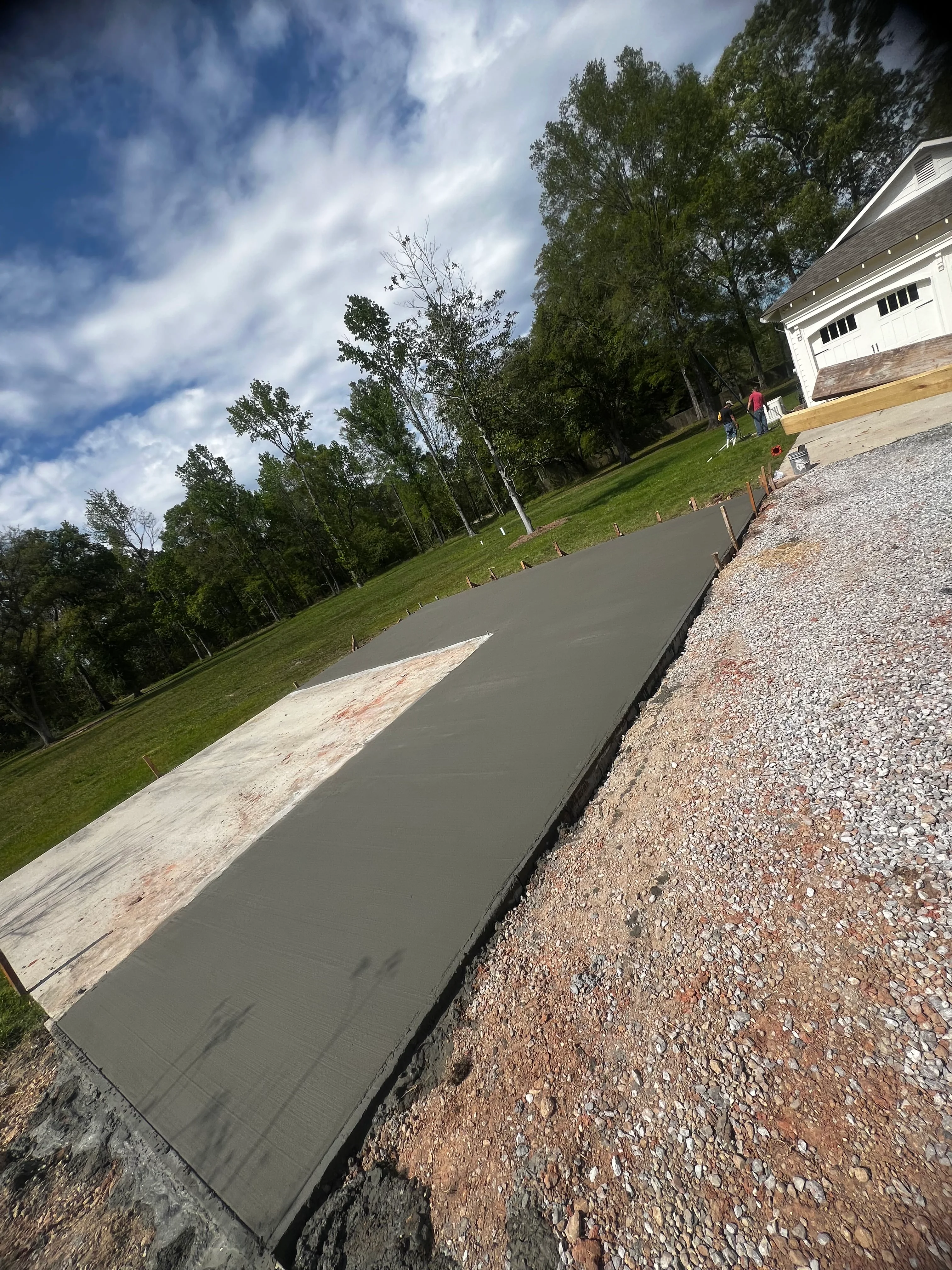 Newly poured concrete driveway with gravel base and residential home in background