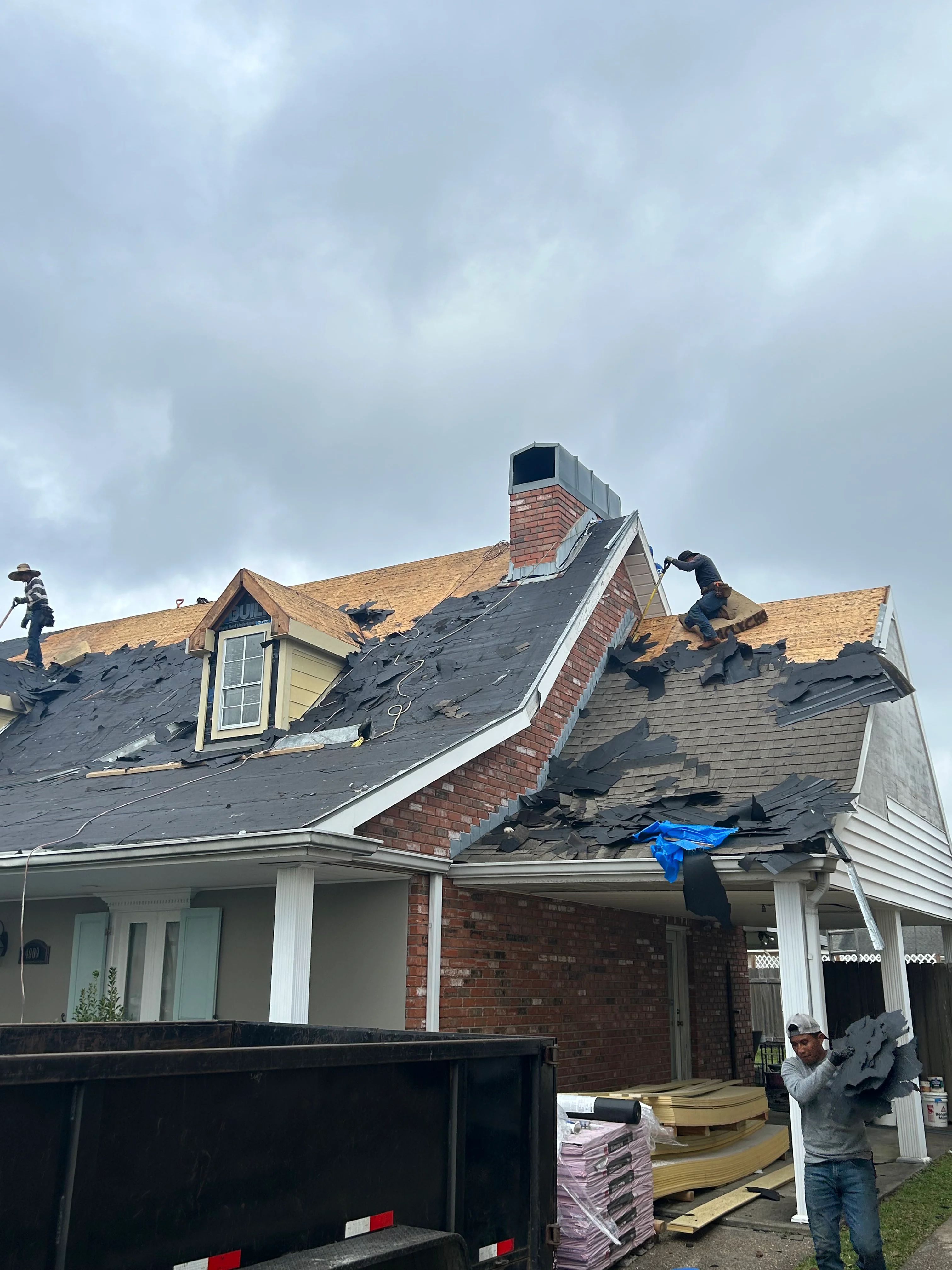 Residential roof replacement in progress with workers installing new shingles on two-story home