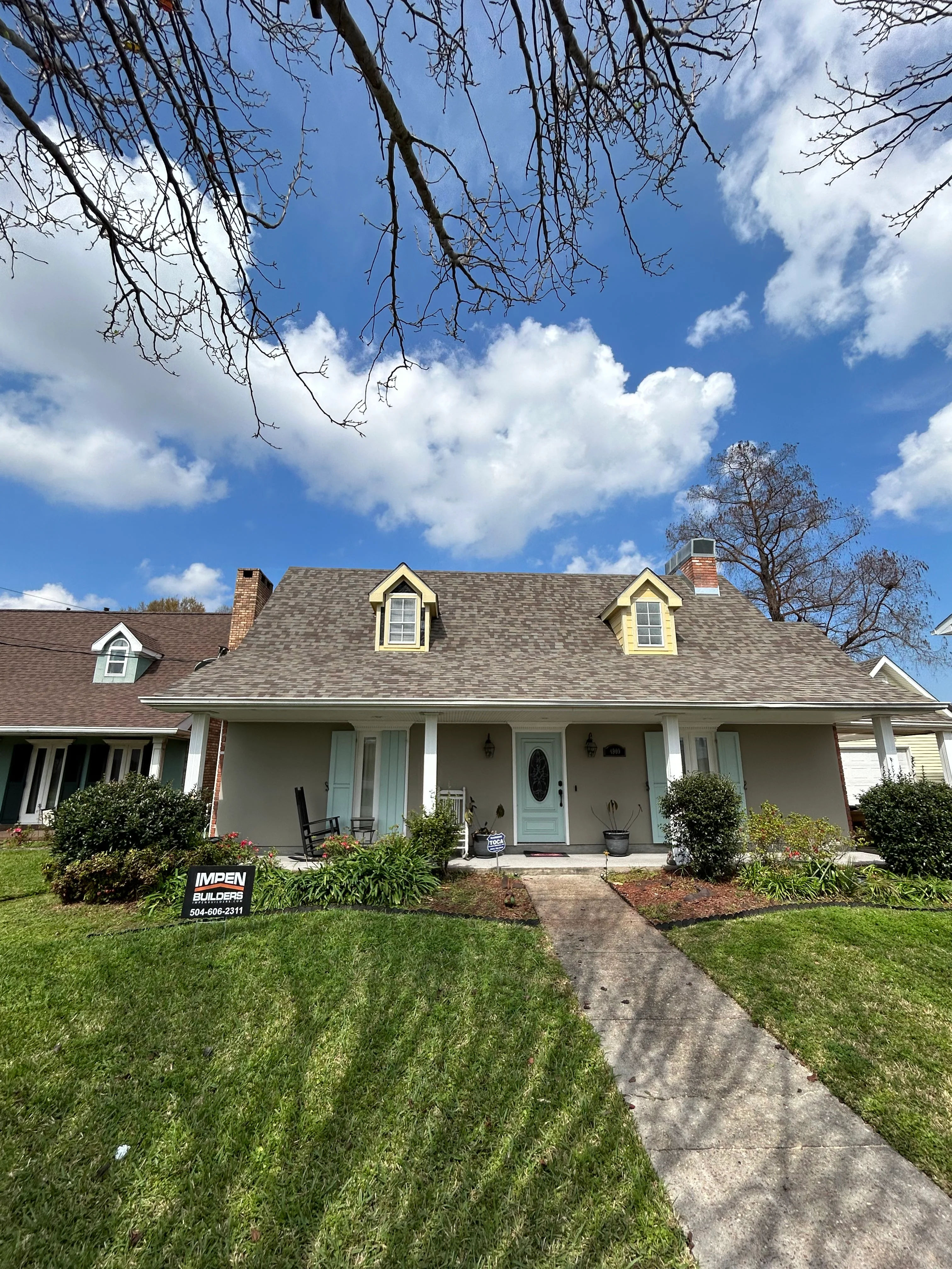 Two-story home with new gray roof, yellow dormers, white trim, and front porch with landscaping