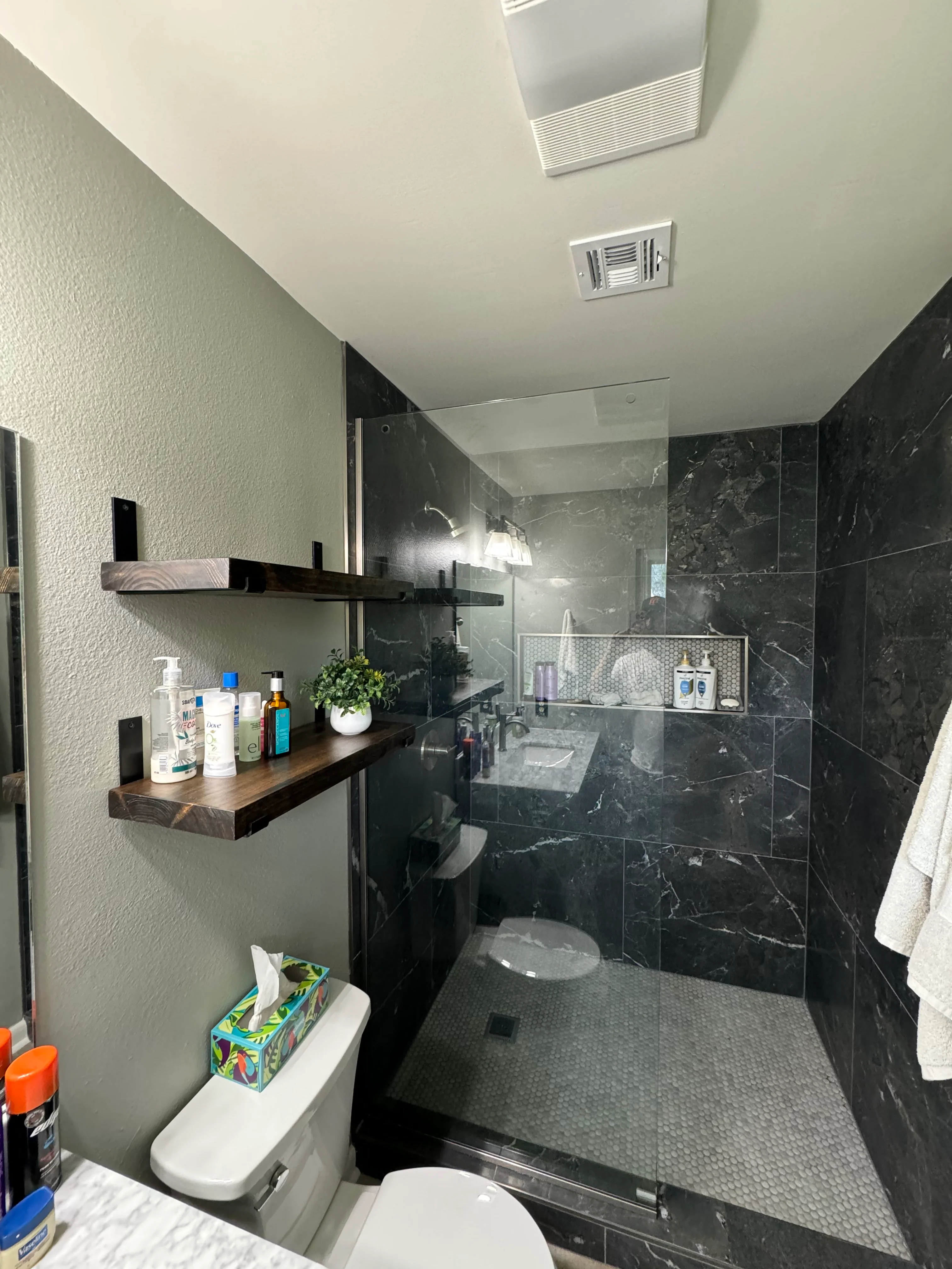 Modern bathroom with black marble tile shower, floating wood shelf, and white textured walls