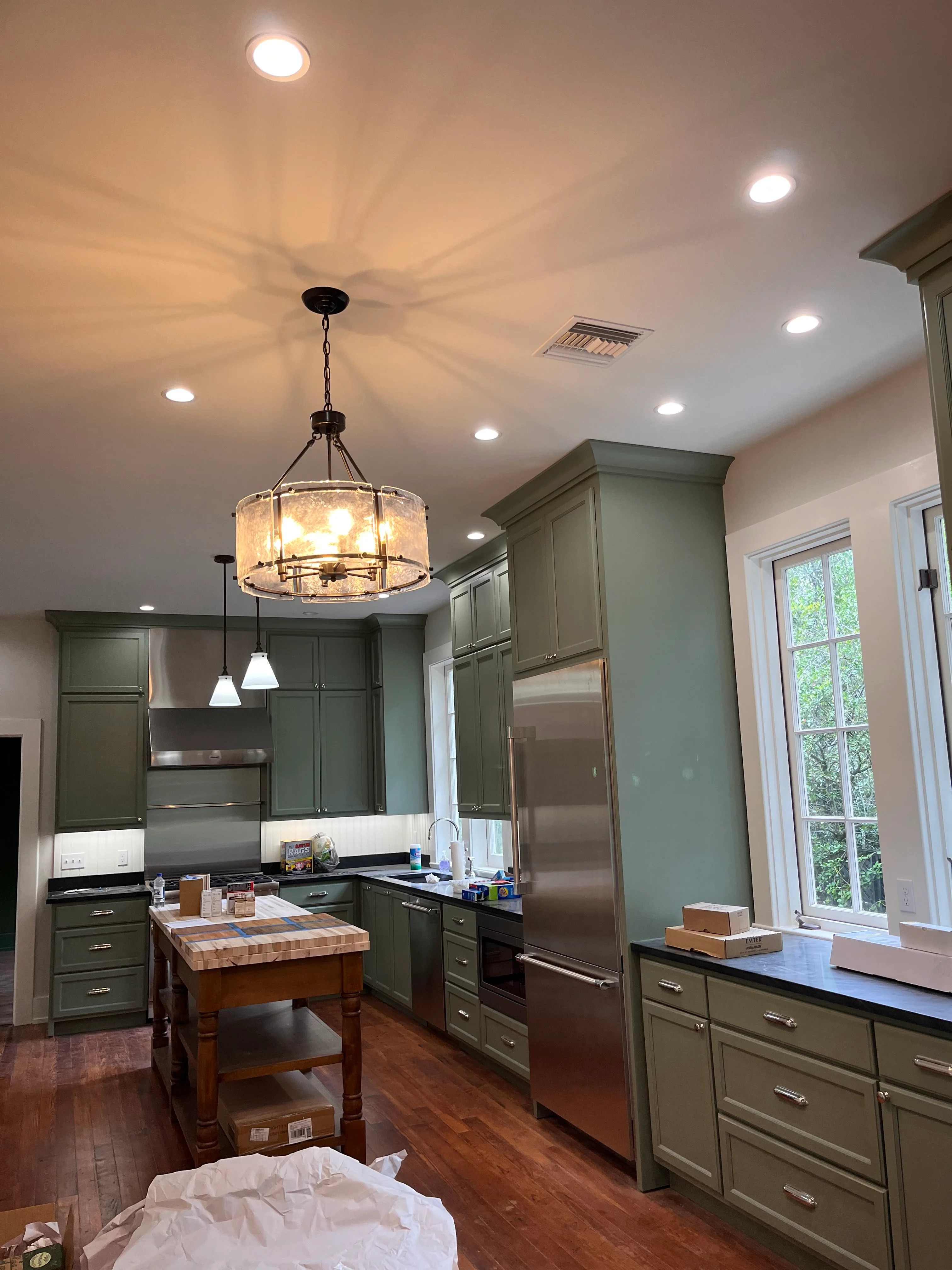 Modern kitchen with sage green cabinets, stainless steel appliances, wood island, and pendant lighting