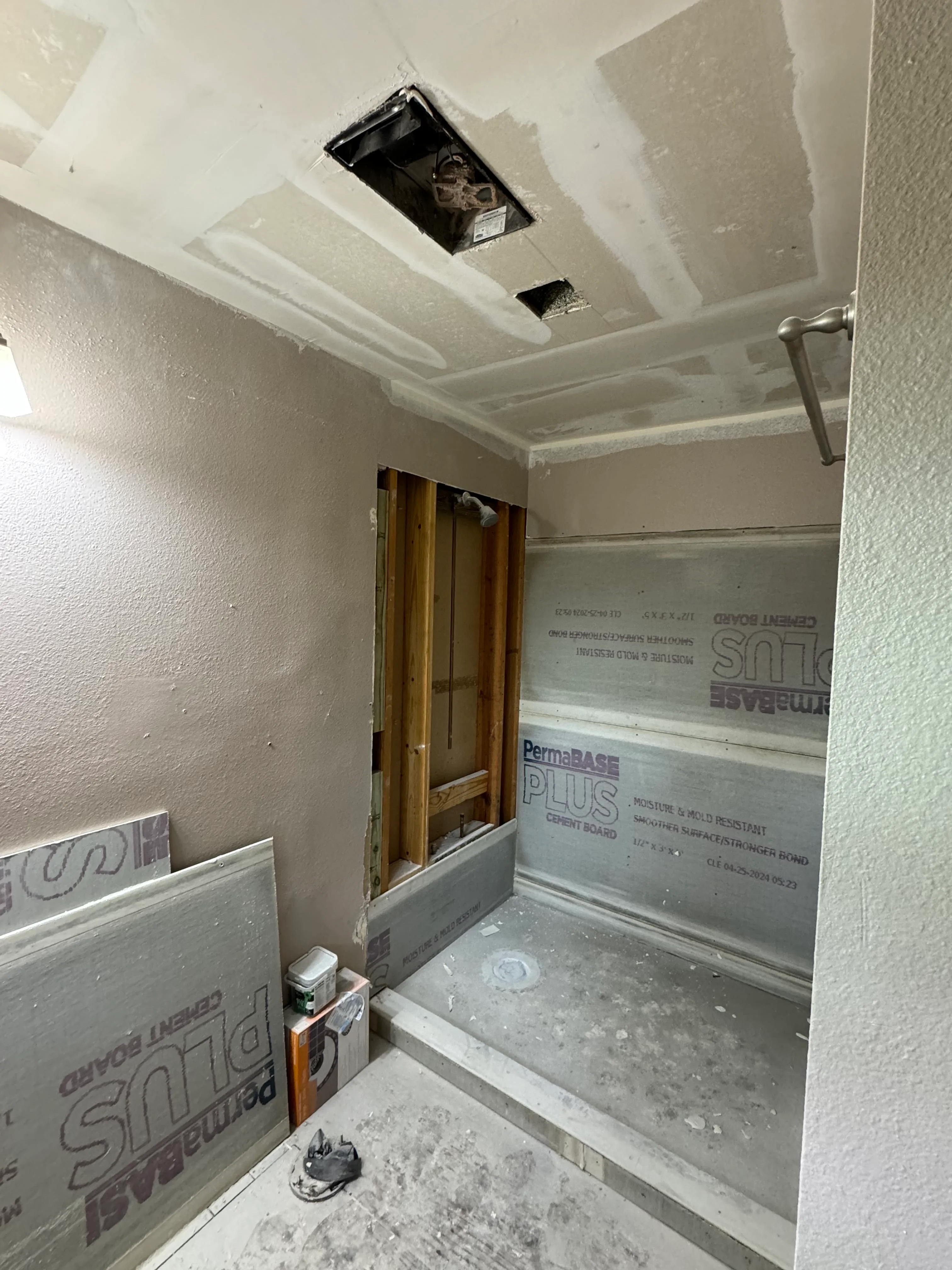 Bathroom under renovation showing drywall ceiling with recessed light opening and cement board walls