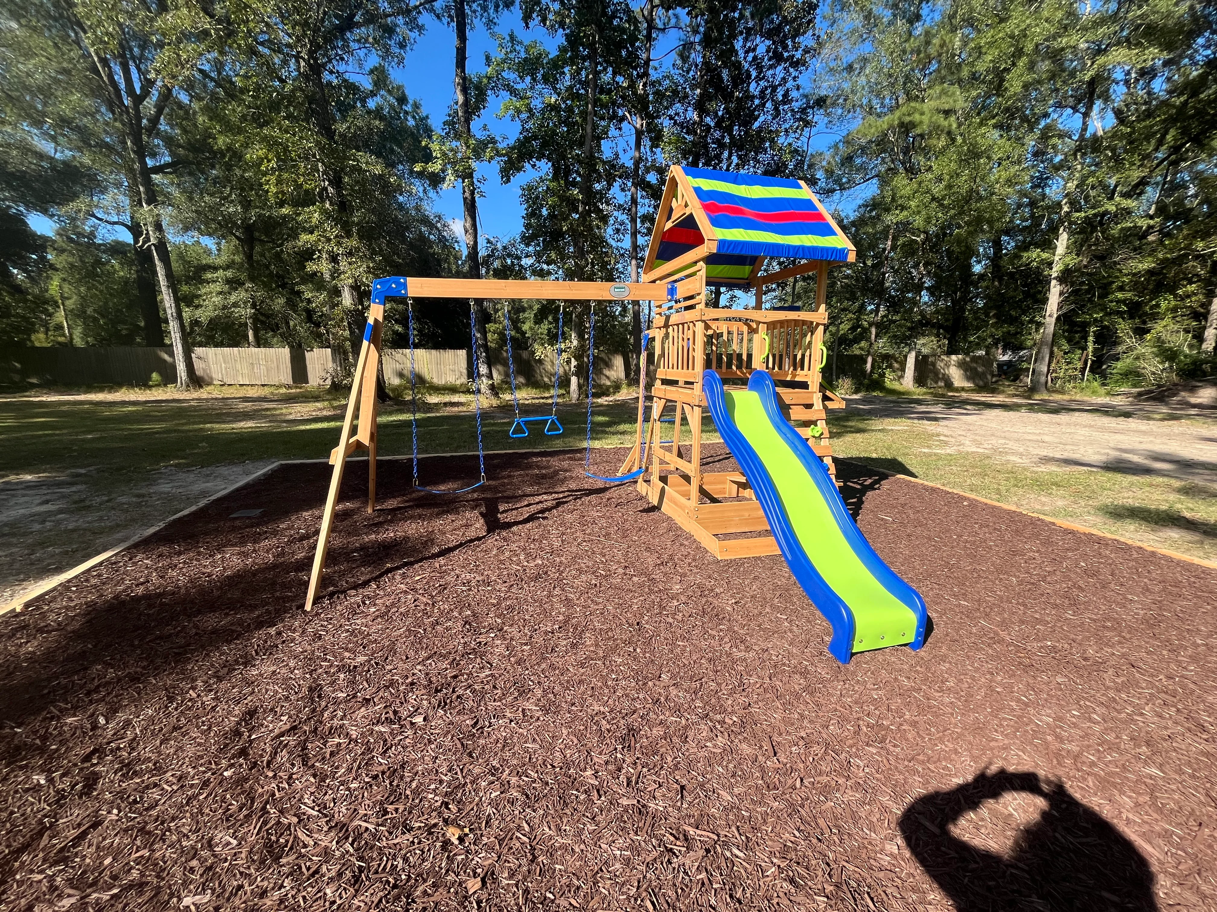 Wooden playground with blue and lime slide, swings, and striped canopy roof on mulch base