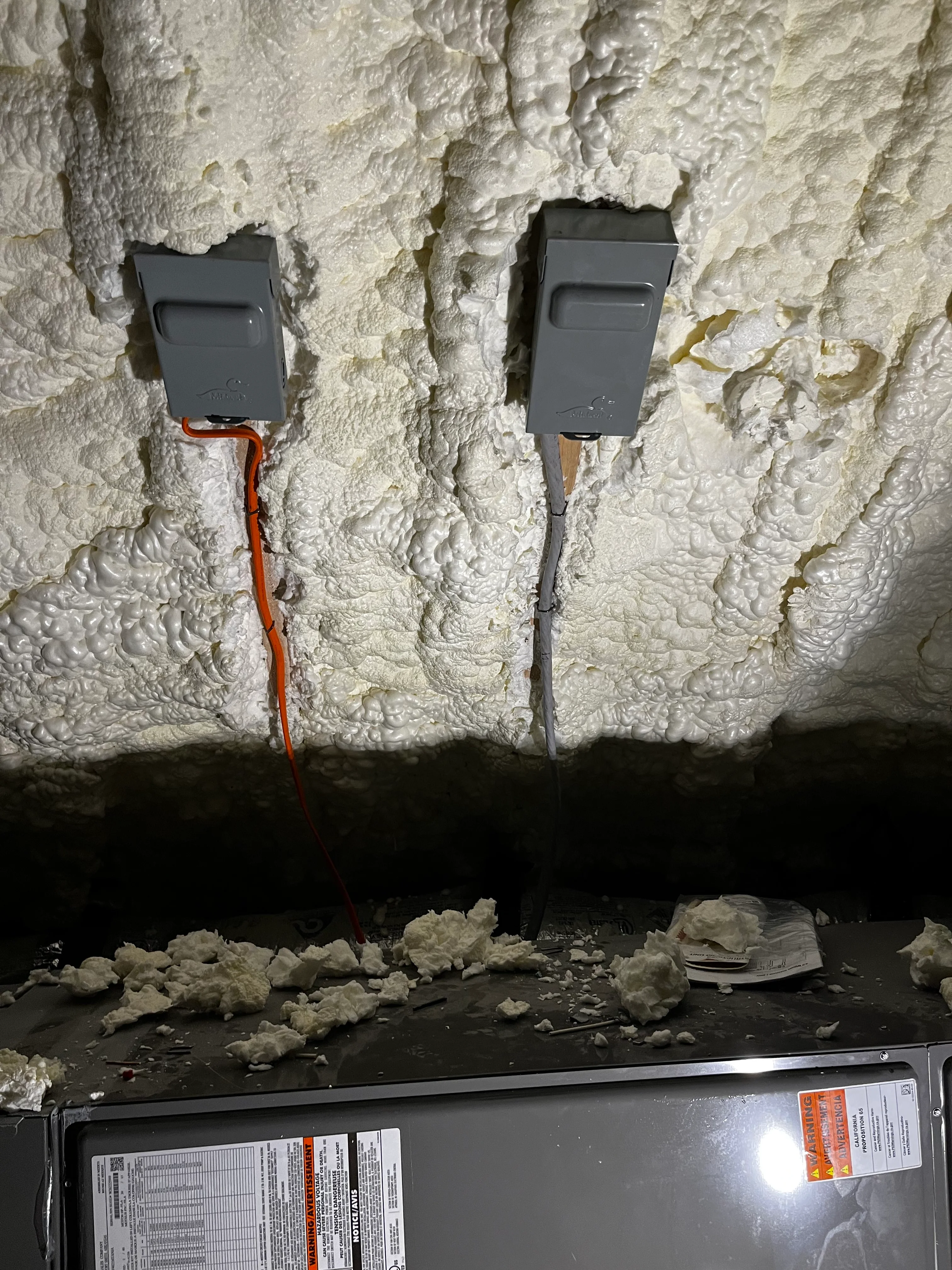 Two gray electrical outlets installed in white spray foam insulation with colored wire conduit