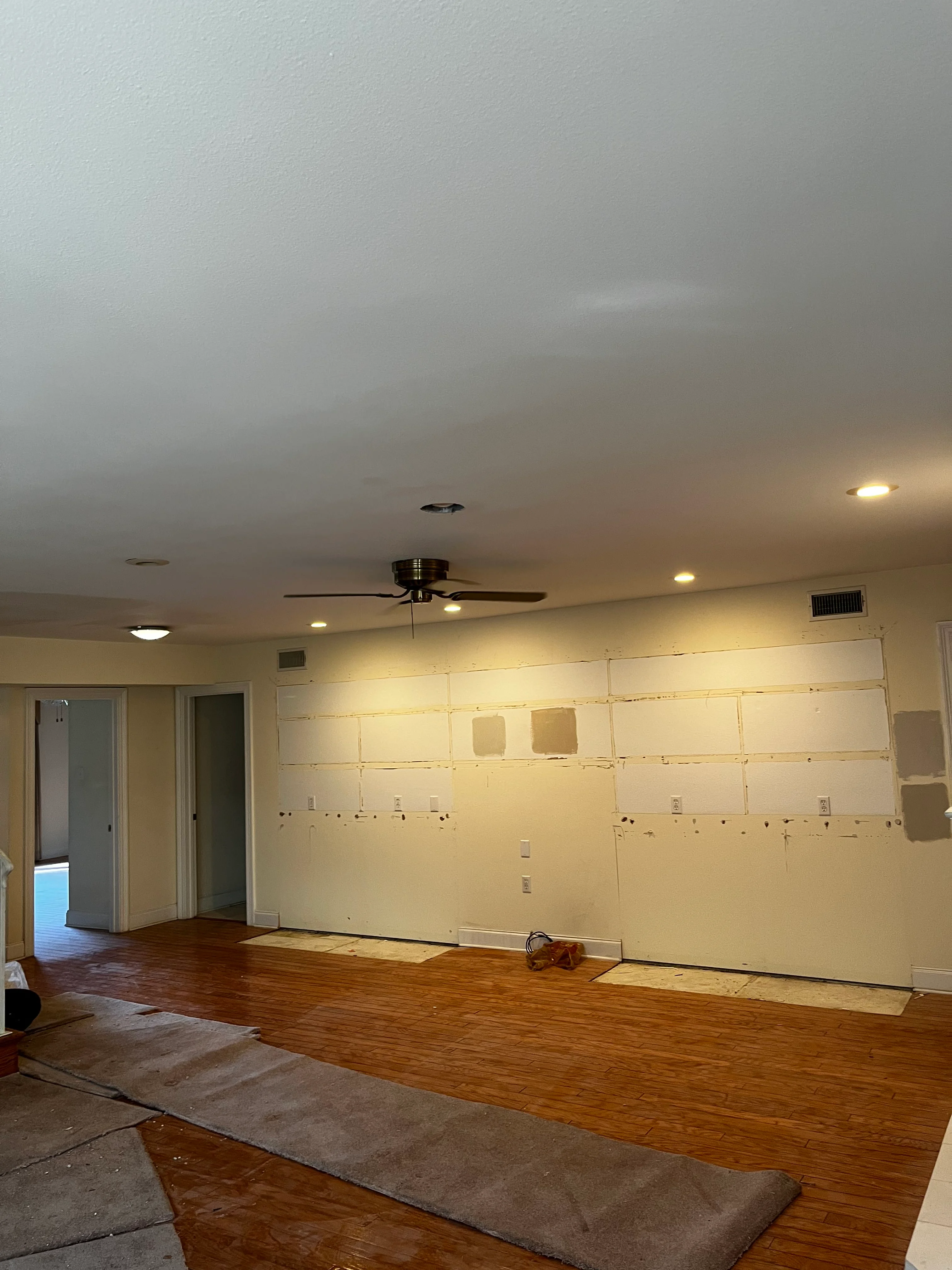 Interior room with newly installed drywall, recessed lighting, and hardwood flooring during renovation