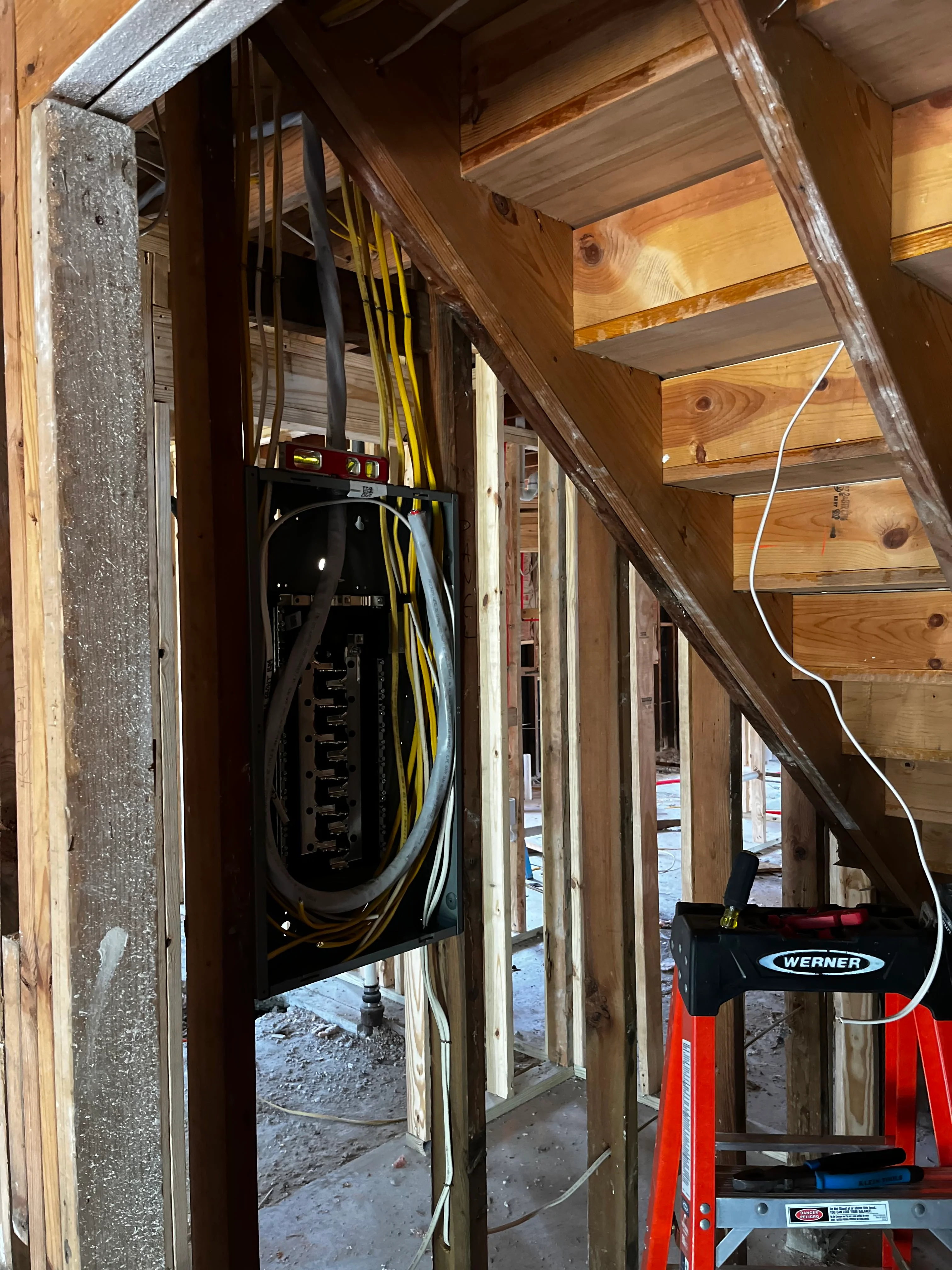 Electrical panel installation with yellow and black service wires in wooden frame construction