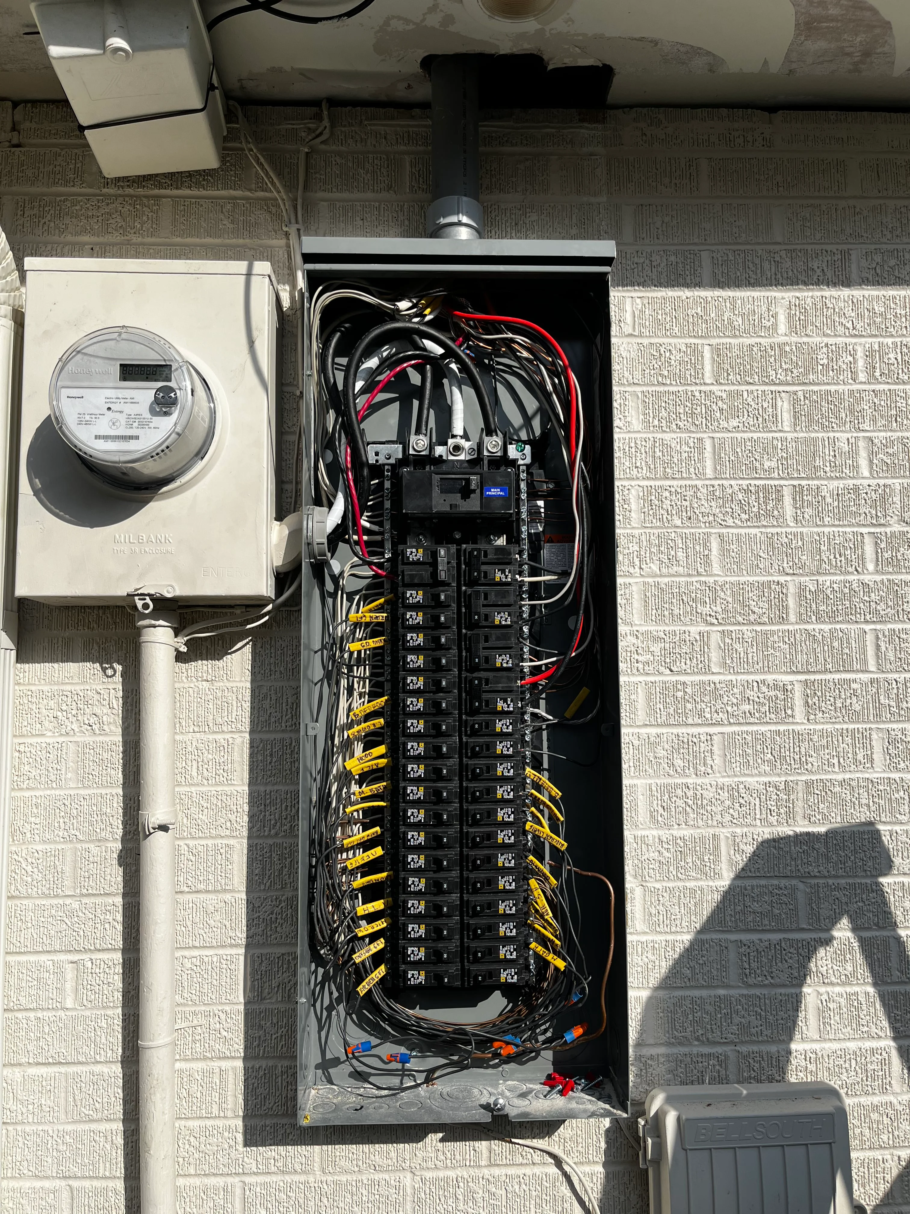 Electrical panel with breakers and organized wiring next to utility meter on brick wall