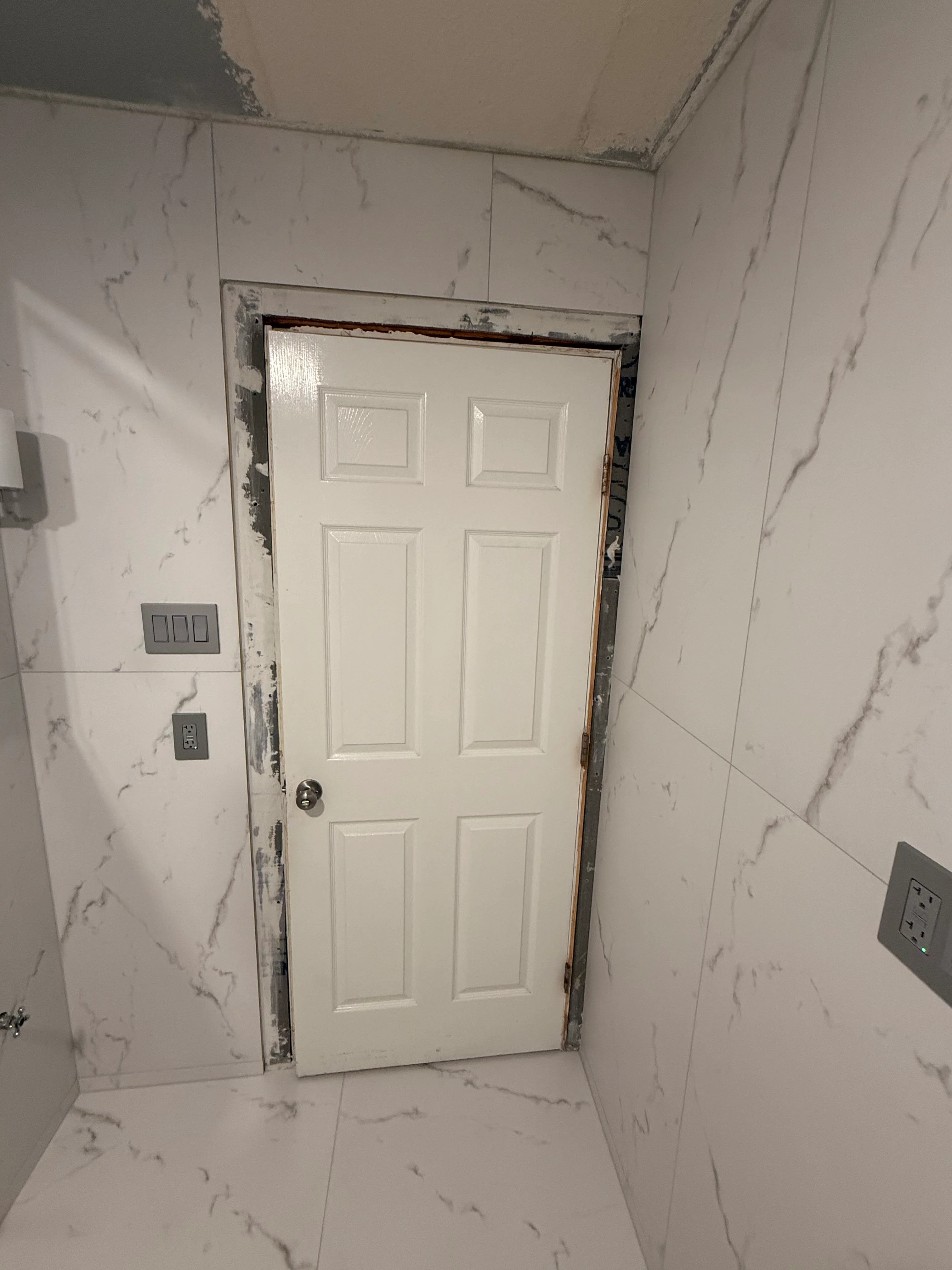 Marble tile bathroom with white six-panel door and updated electrical fixtures