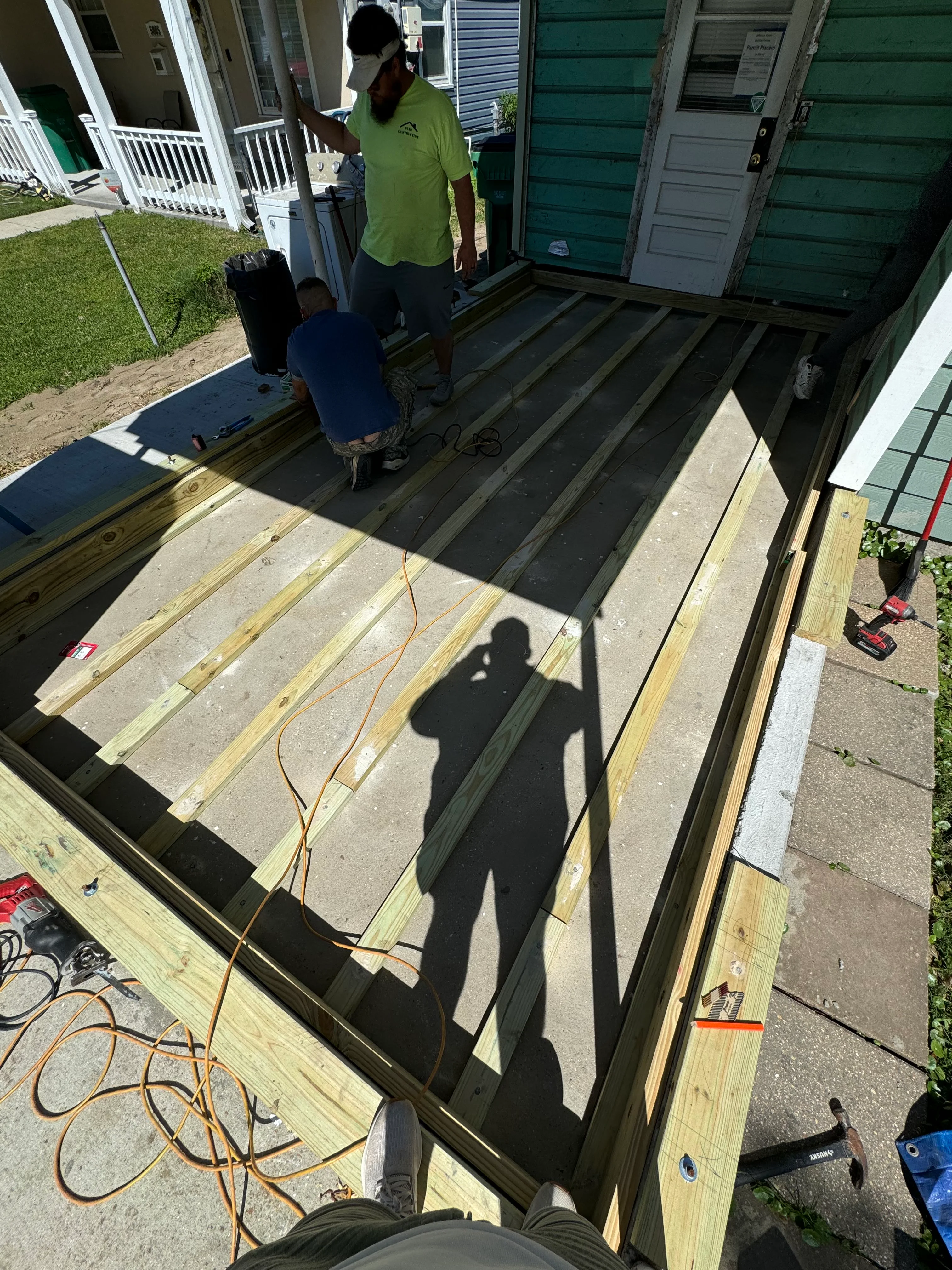 Workers installing black composite decking boards over new pressure-treated lumber frame on residential deck