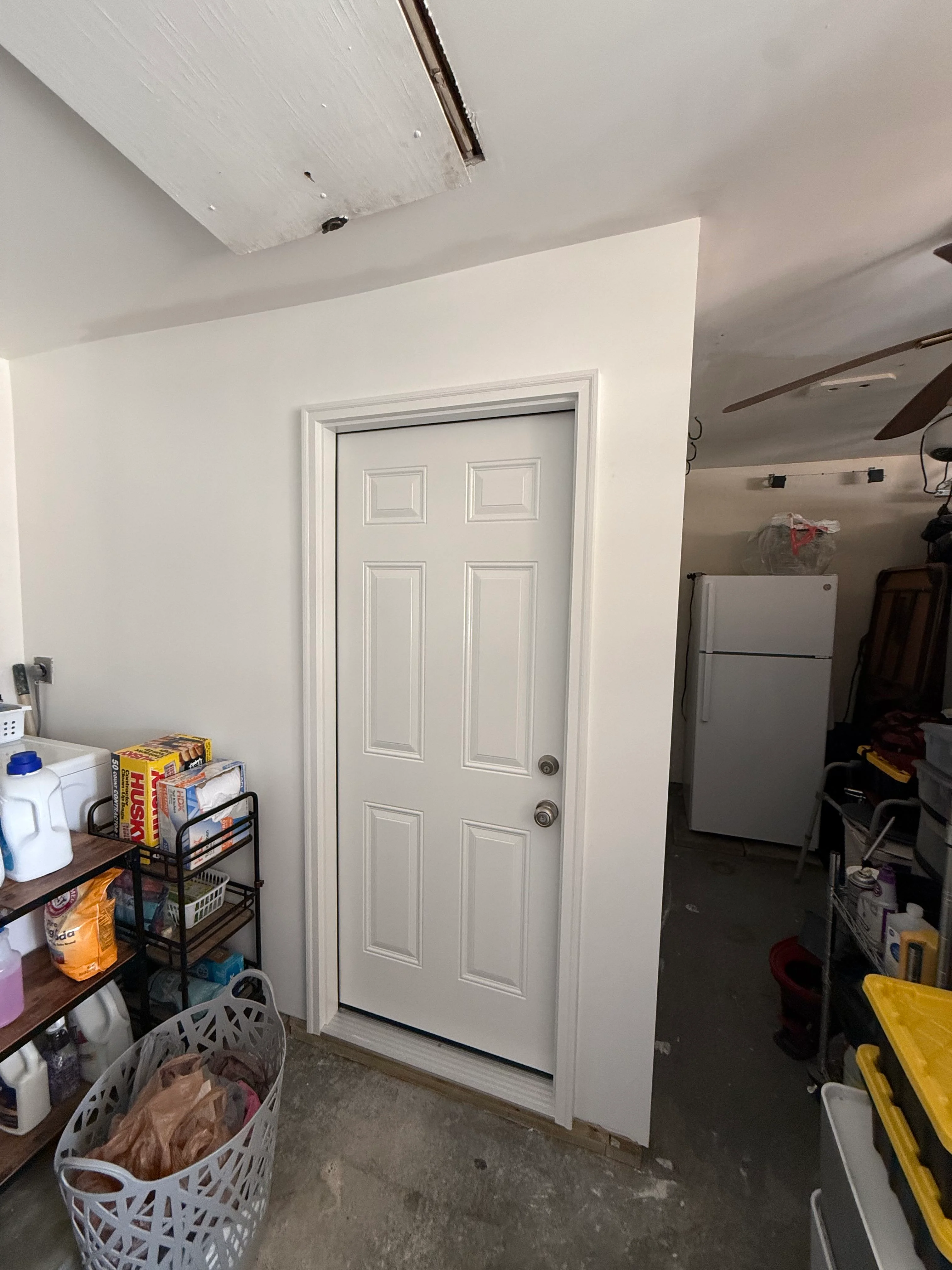 Newly renovated garage with white drywall, six-panel door, and finished ceiling