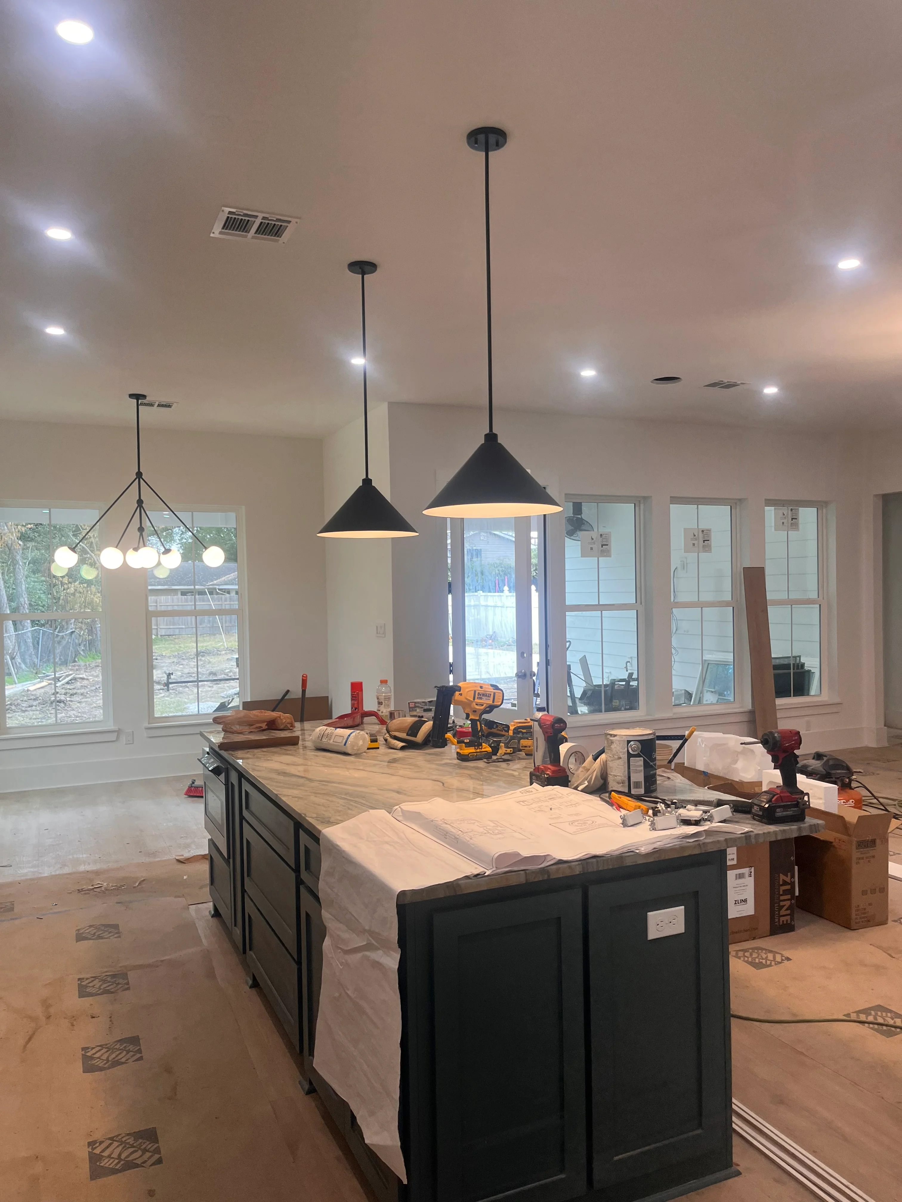 Kitchen renovation in progress with black island, pendant lights, and large windows