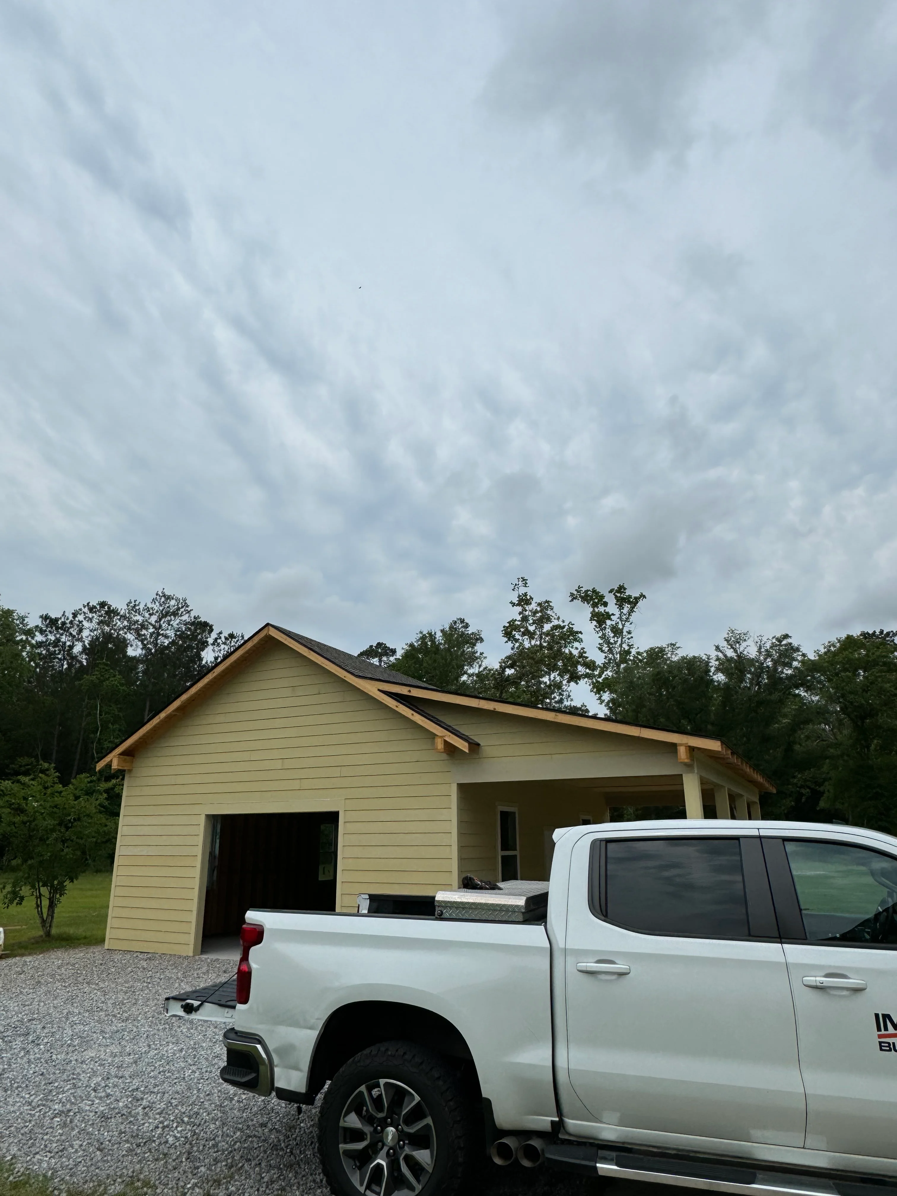 Newly constructed cream-colored garage with covered porch and pitched roof in rural setting