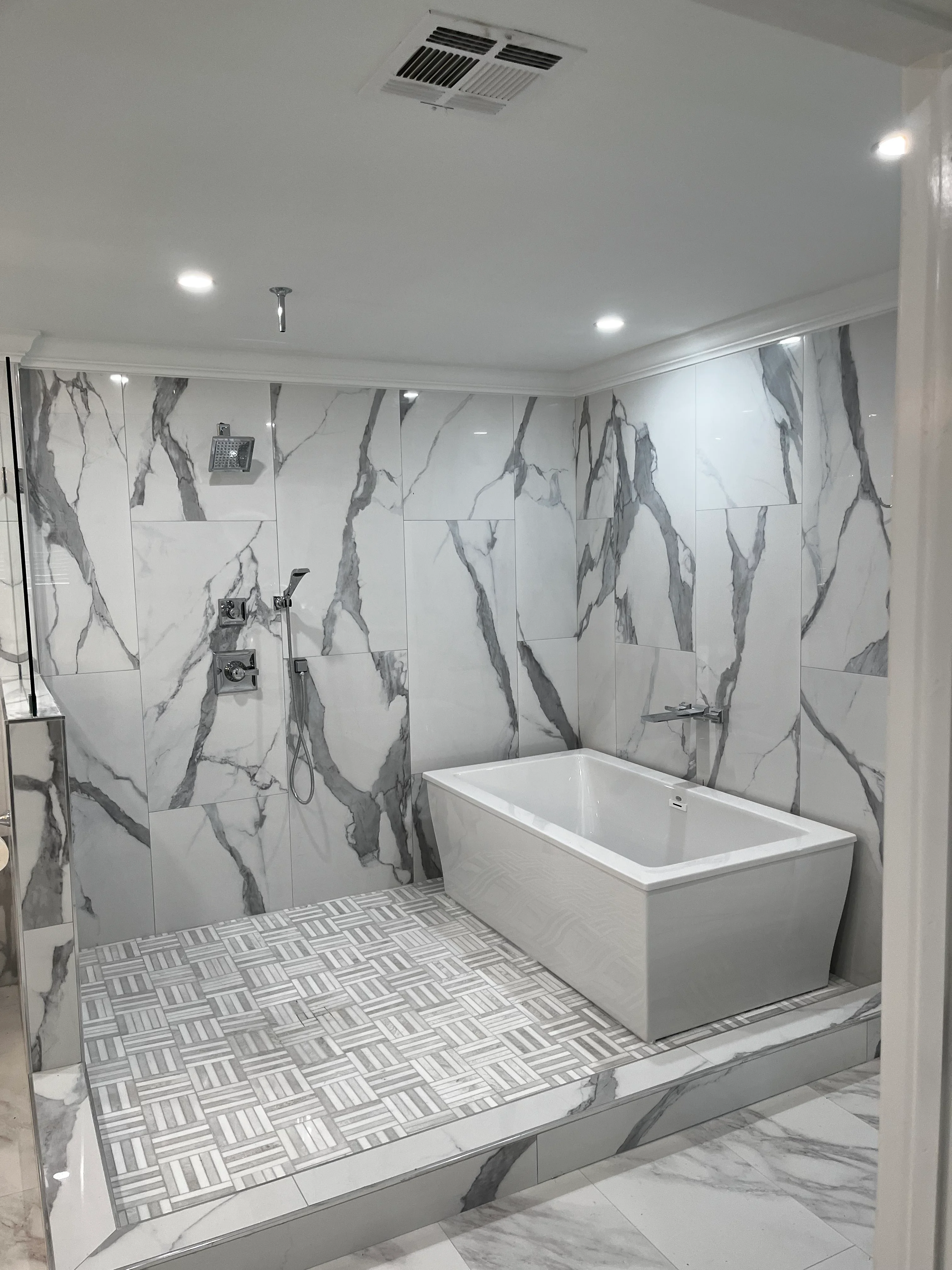 Modern master bathroom with marble tile shower, freestanding tub, and geometric floor pattern
