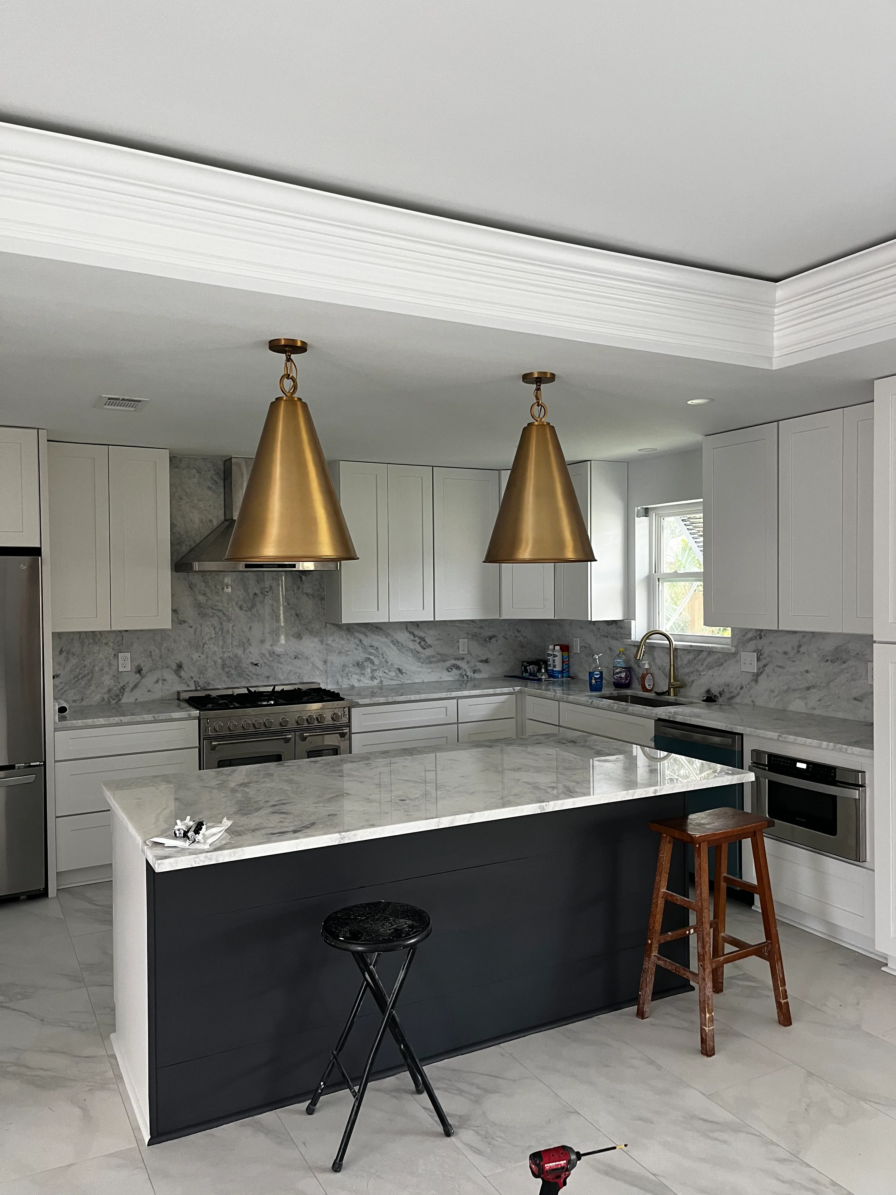Modern kitchen with white cabinets, marble counters, black island, and brass pendant lights