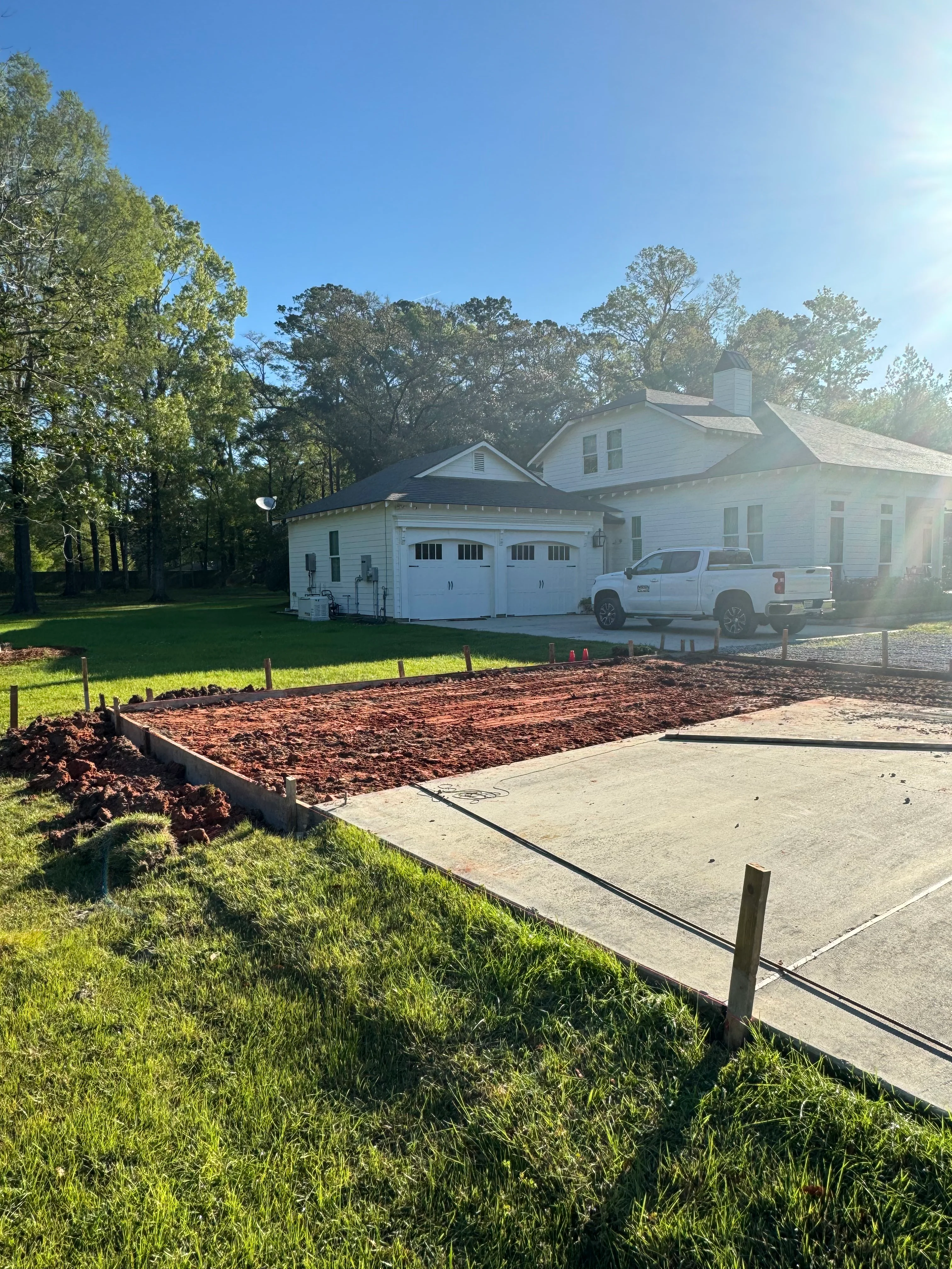 White farmhouse with attached garage, concrete driveway, and mulched landscaping beds