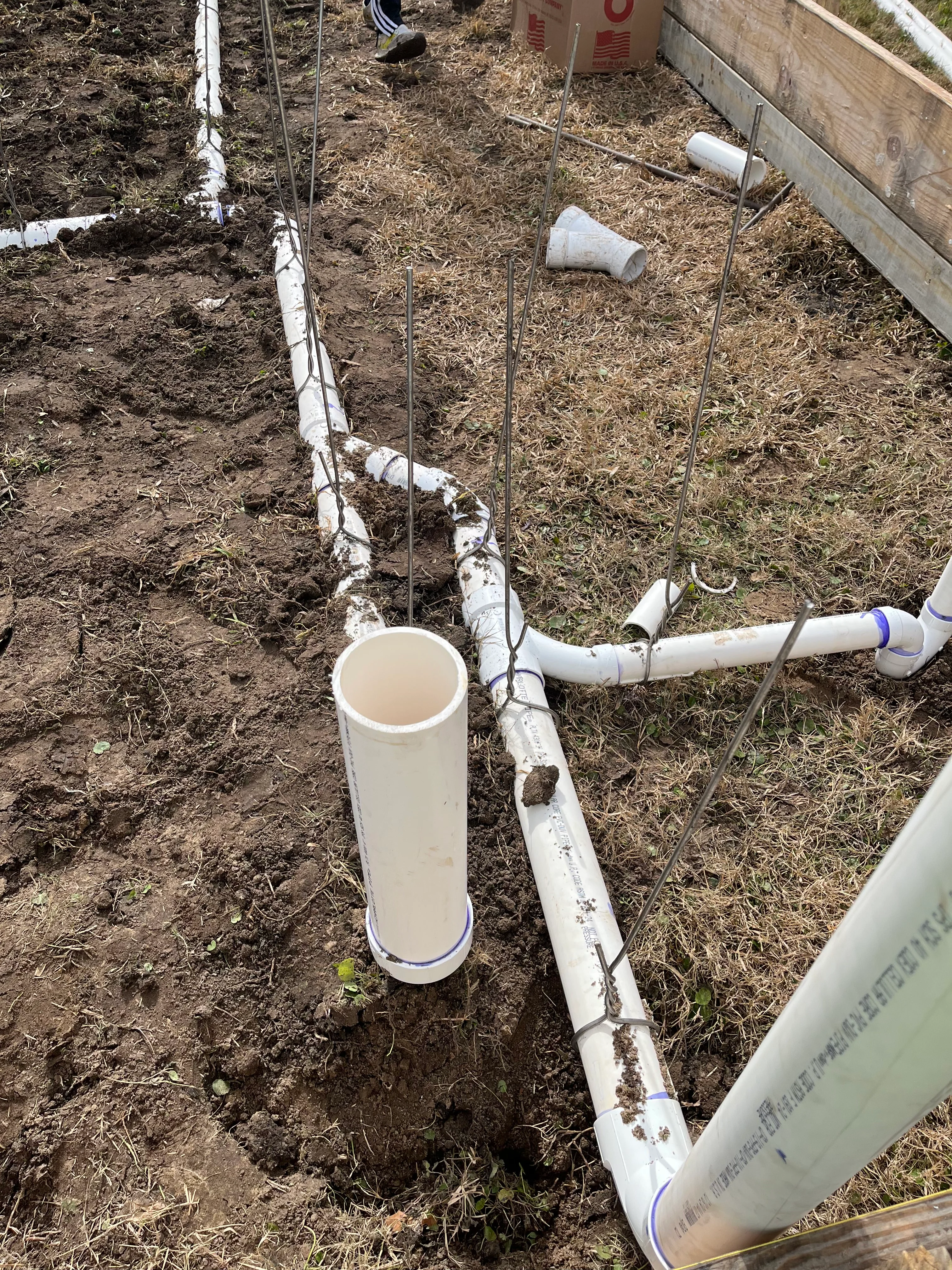 Underground PVC pipe installation with white conduit lines and fittings in excavated soil trench