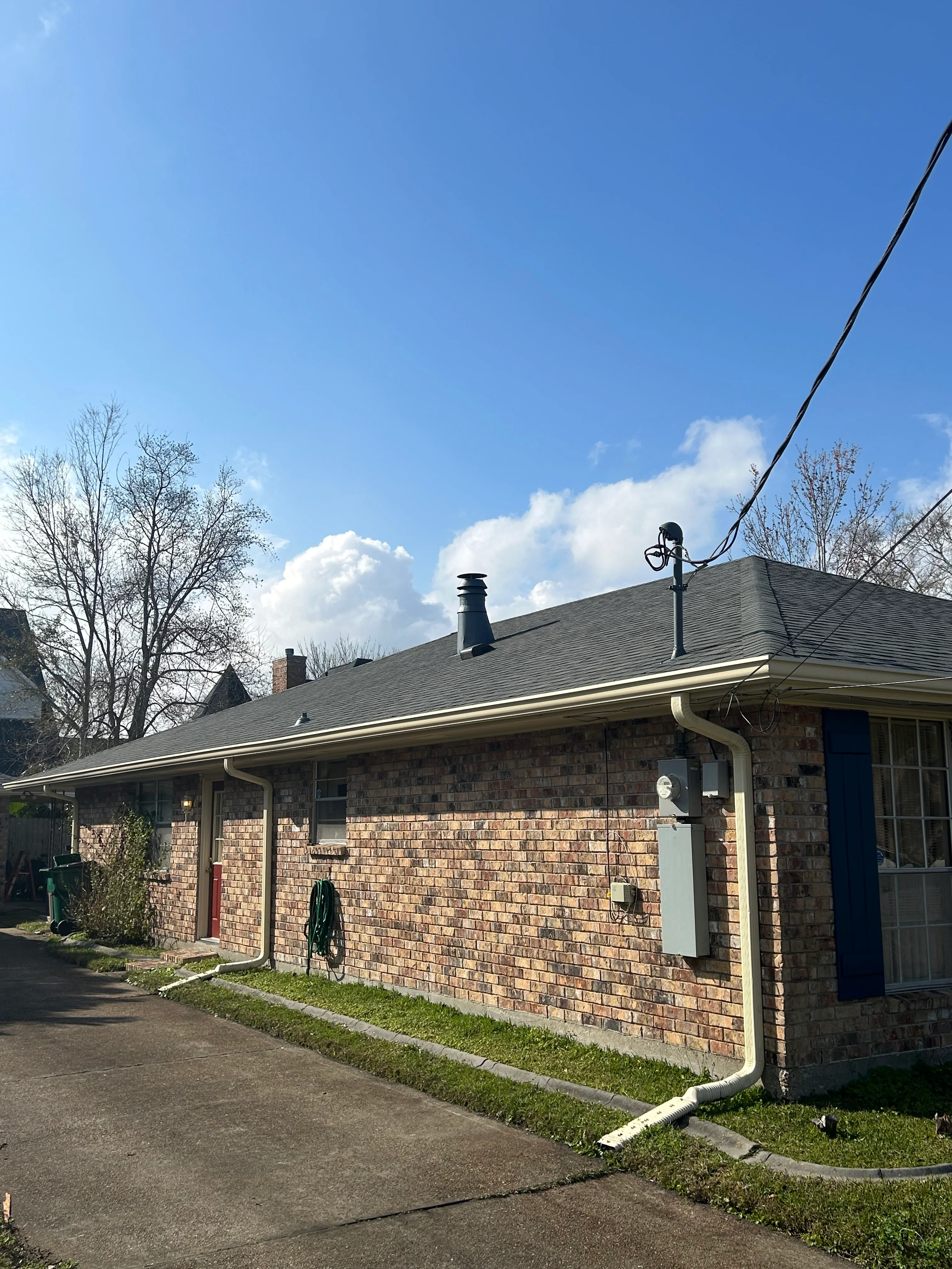 Brick home with new gray roof shingles and white gutter system installed