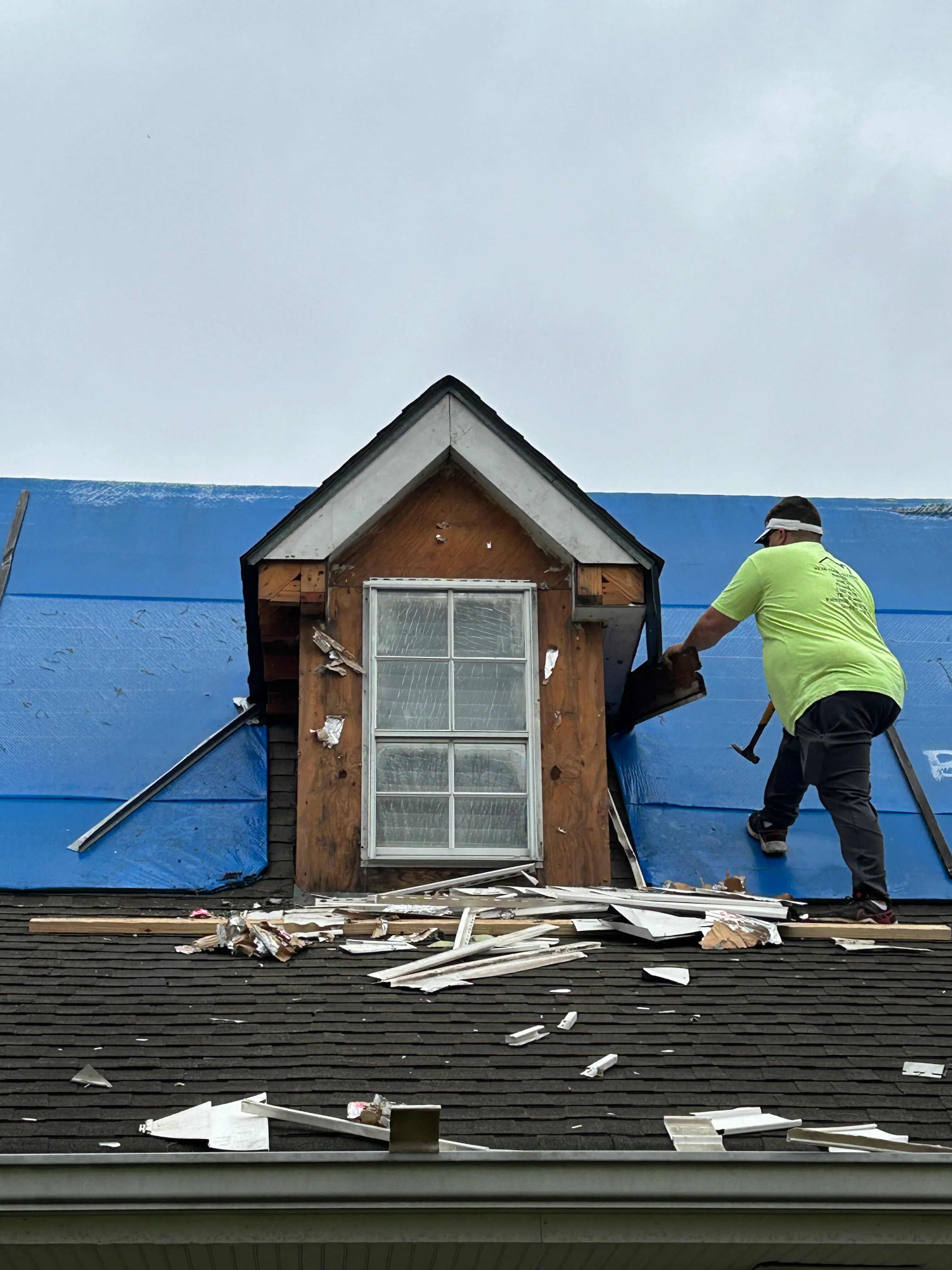 Worker installing new window in reconstructed roof dormer with blue protective covering